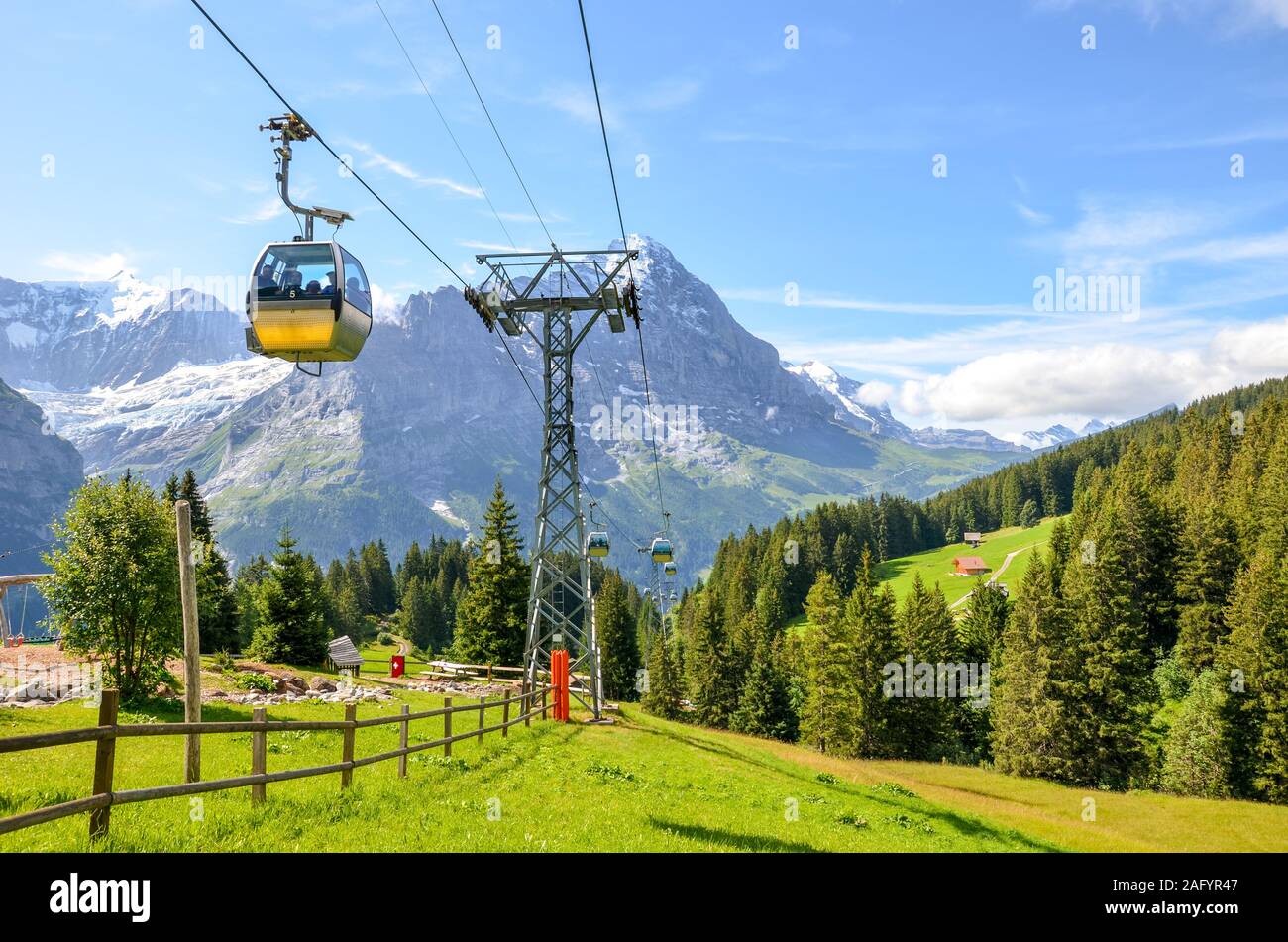 Câble jaune voiture dans les Alpes suisses. Gondola allant de Grindelwald en premier dans la région de la Jungfrau. Paysage alpin d'été avec des montagnes aux sommets enneigés en arrière-plan. Transport de touristes en amont. Banque D'Images