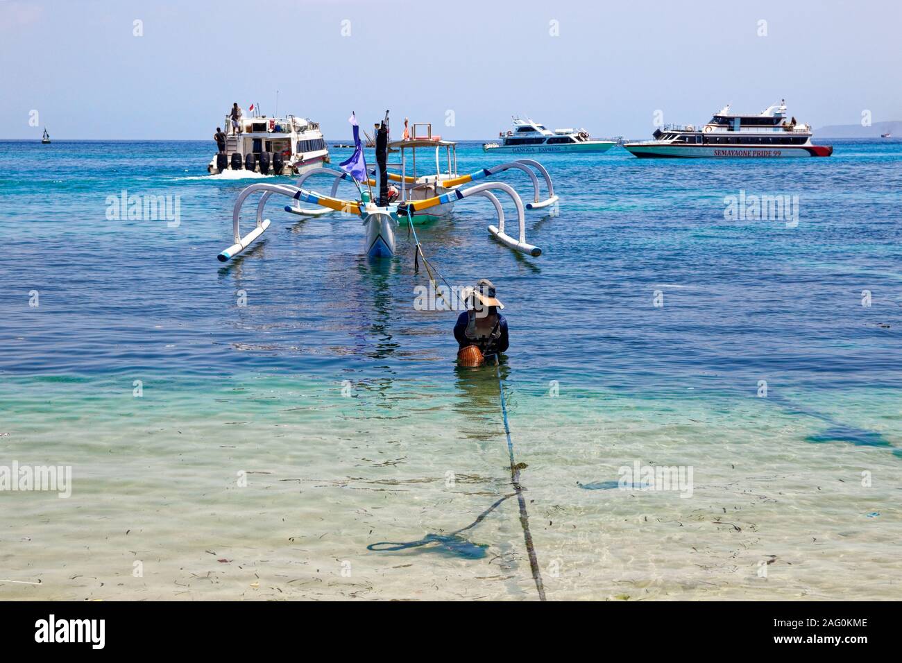 Habituellement jour de travail de l'homme dans l'eau ancrage de la coquille en bois, debout dans les eaux de la mer balinaise Banque D'Images