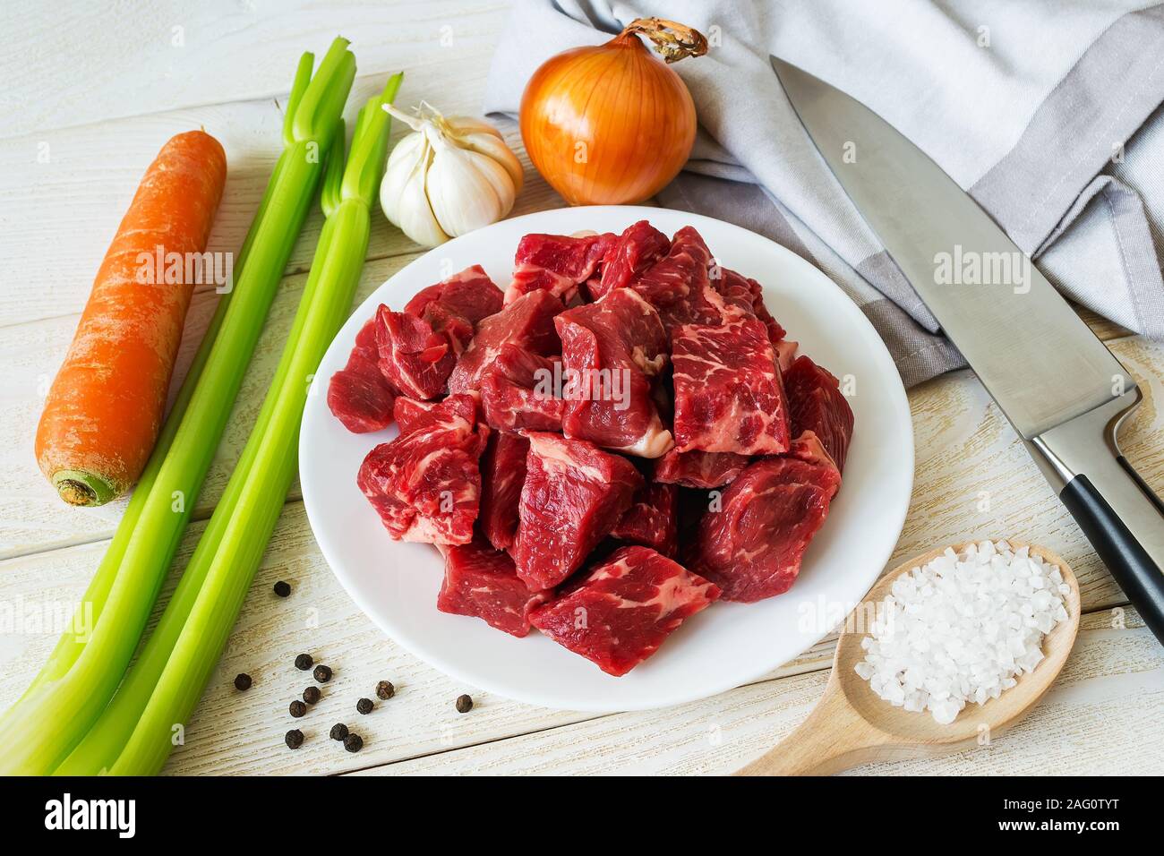 Ingrédients de base pour la cuisson à l'étuvée ou viande goulash : morceaux de bœuf frais, les carottes, les oignons, l'ail, le céleri et le sel sur la table en bois blanc. Faire cuire à la maison. Banque D'Images