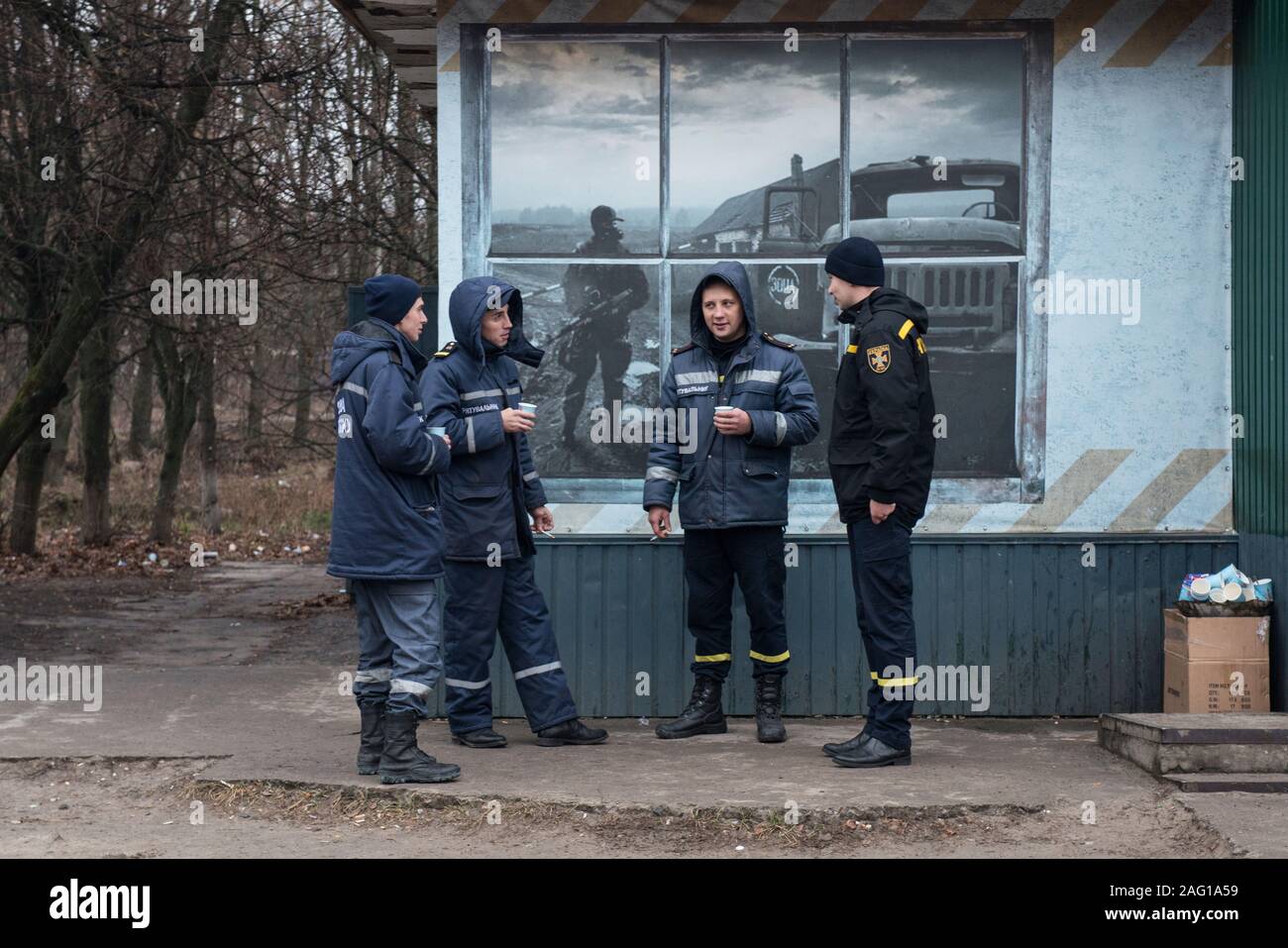 Employés de la centrale nucléaire de Tchernobyl ayant une pause-café pendant leur garde à l'extérieur d'un bar à Tchernobyl à la ville. Dans l'arrière-plan est vu une peinture murale représentant un syndic de la zone après la catastrophe nucléaire en avril 1986. Tchernobyl (ville), zone d'exclusion de Tchernobyl, Ivankiv, Kiev Kiev oblast, Ukraine, Europe de l'Est Banque D'Images