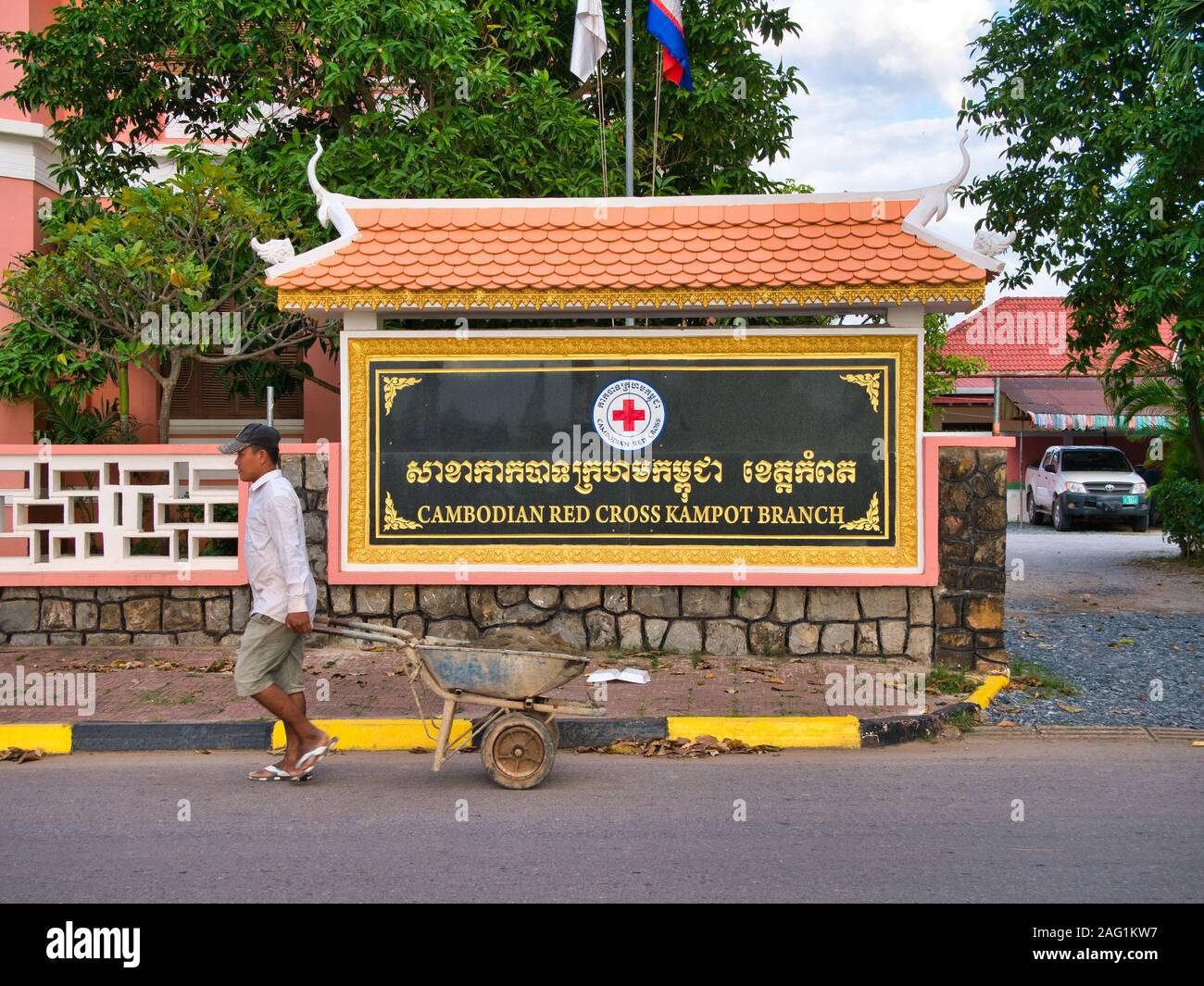 Un travailleur avec une brouette passe le signe extérieur de la Direction générale de Kampot de la Croix-Rouge cambodgienne Banque D'Images