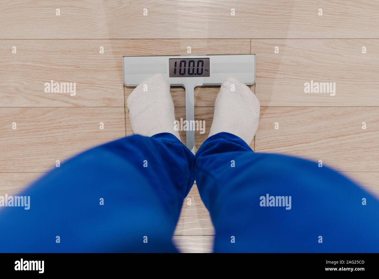 Un homme pesant lui-même sur une échelle numérique habillé en pyjama bleu et blanc chaussettes. Problème de l'embonpoint. Concept de régime. Banque D'Images