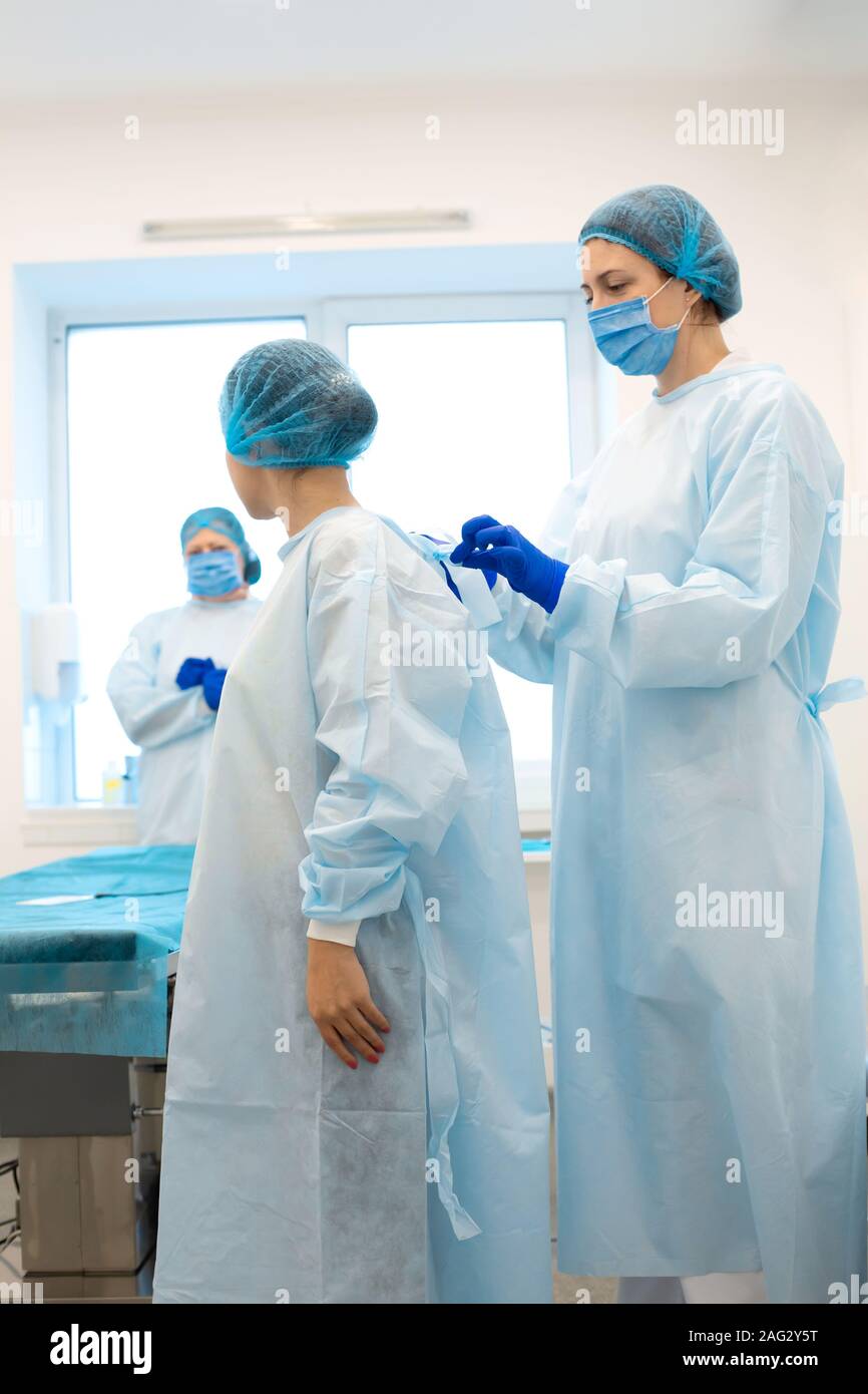 Une infirmière robes une chirurgien dans un costume stérile avant la chirurgie. Banque D'Images