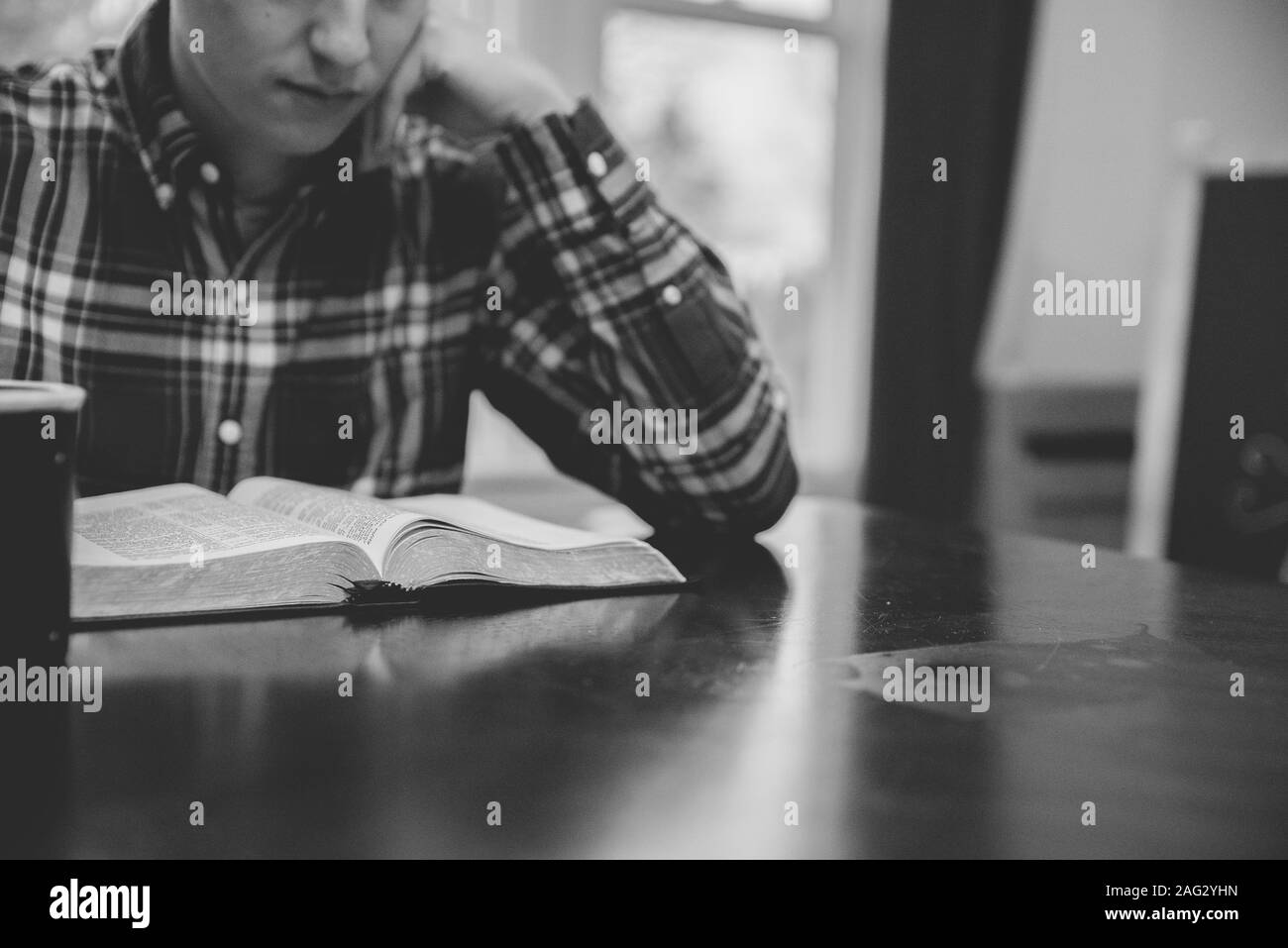 Gros plan d'un homme assis dans un café lisant la bible en noir et blanc Banque D'Images