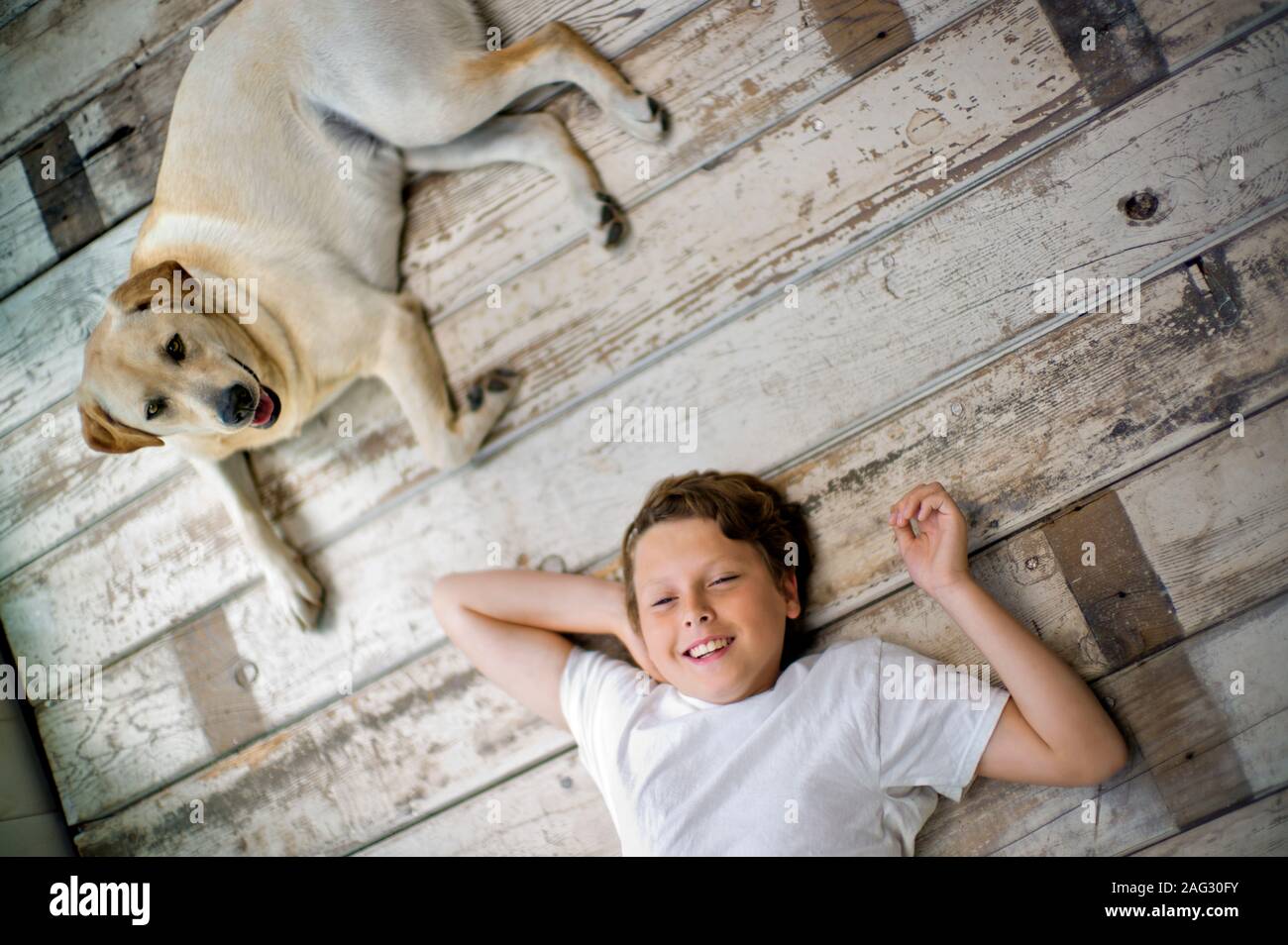 Portrait of a smiling students avec les mains derrière sa tête sur un plancher de bois franc à côté de son chien. Banque D'Images