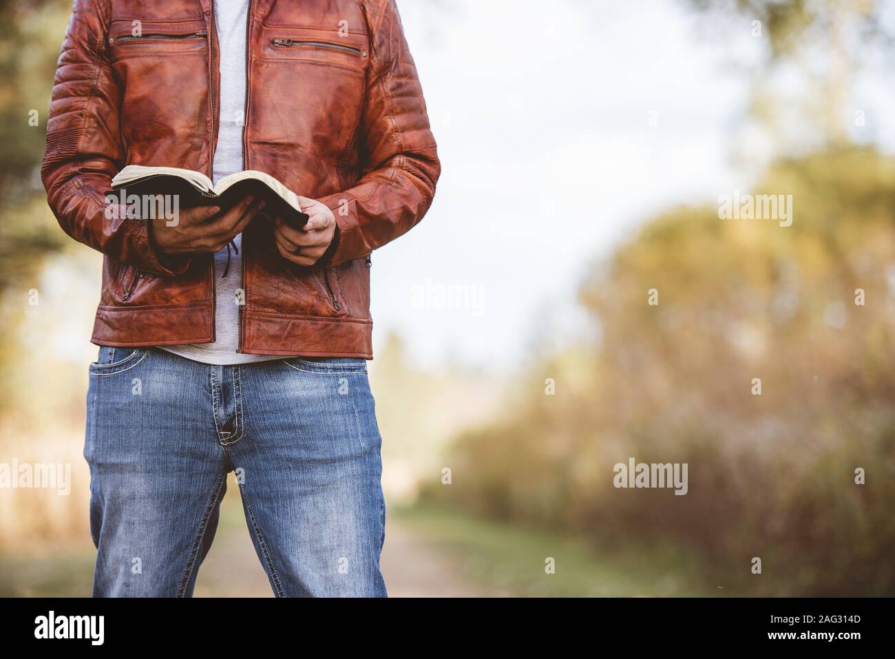 Homme portant une veste en cuir debout sur une route vide et la lecture de la bible avec un arrière-plan flou Banque D'Images