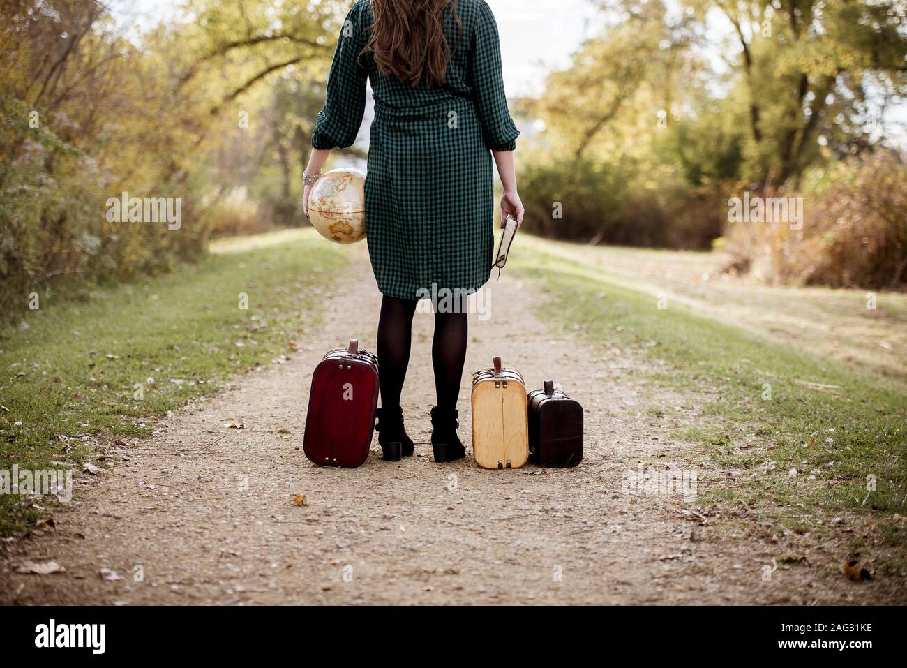 Une femme se tenant entre ses vieilles valises tout en tenant un bureau globe et la bible Banque D'Images