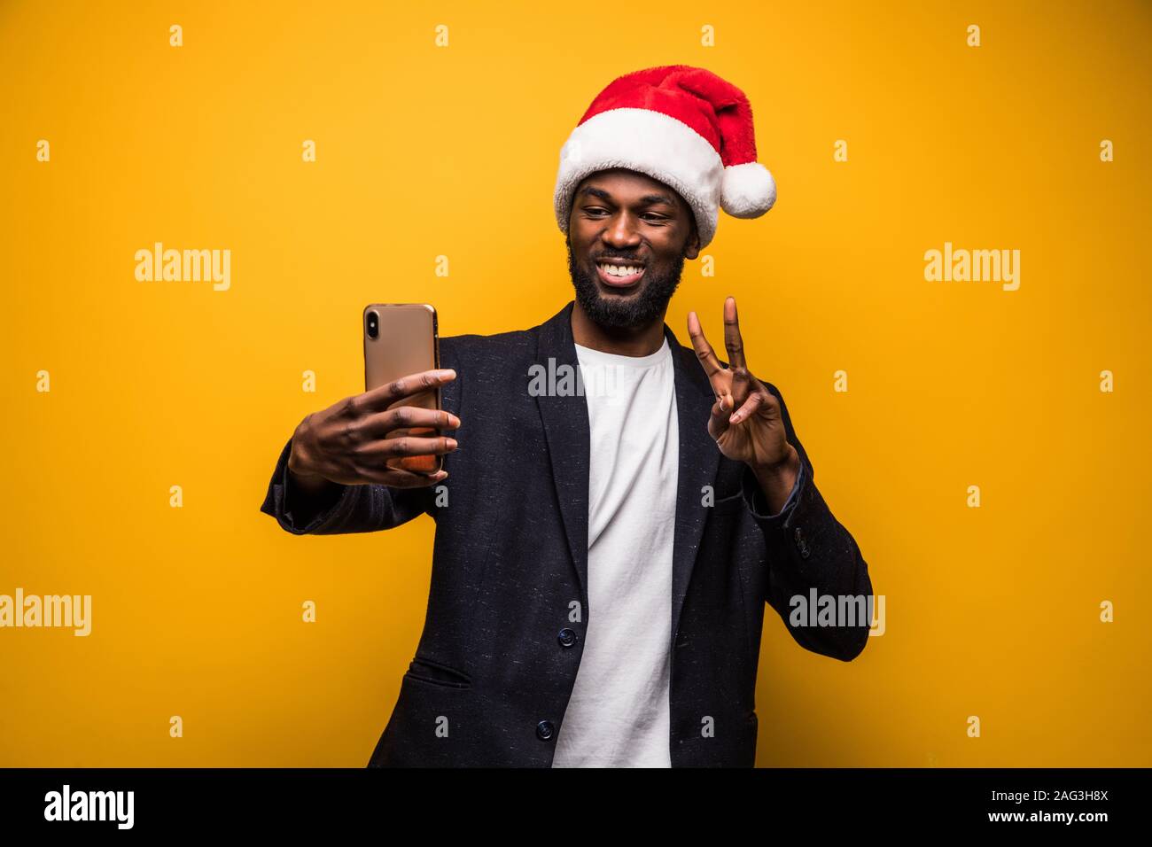 Jeune homme africain à santa hat prendre le téléphone en selfies isolé sur fond jaune Banque D'Images