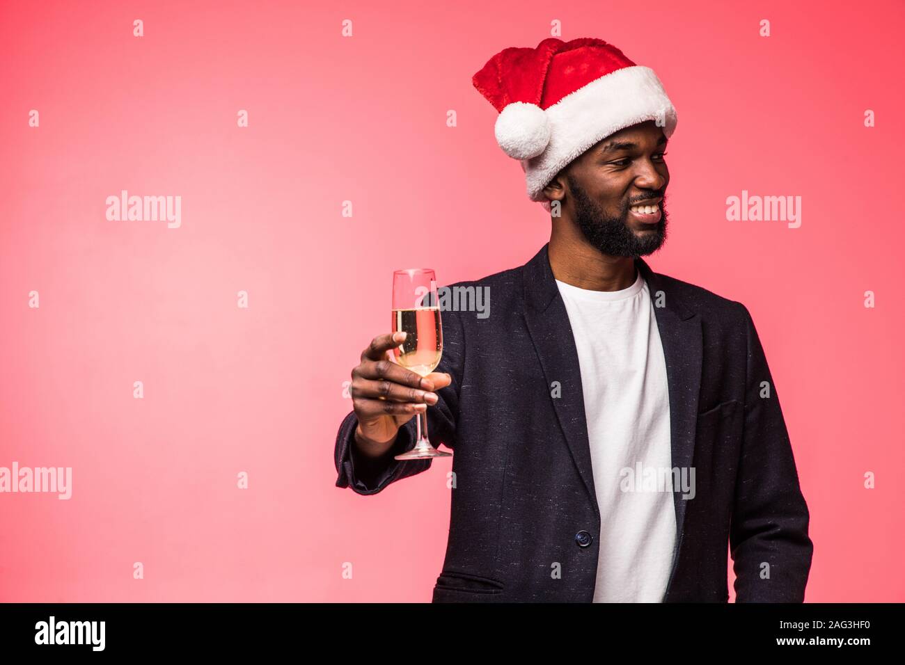 Jeune homme africain à santa hat drinking champagne sur fond rouge Banque D'Images