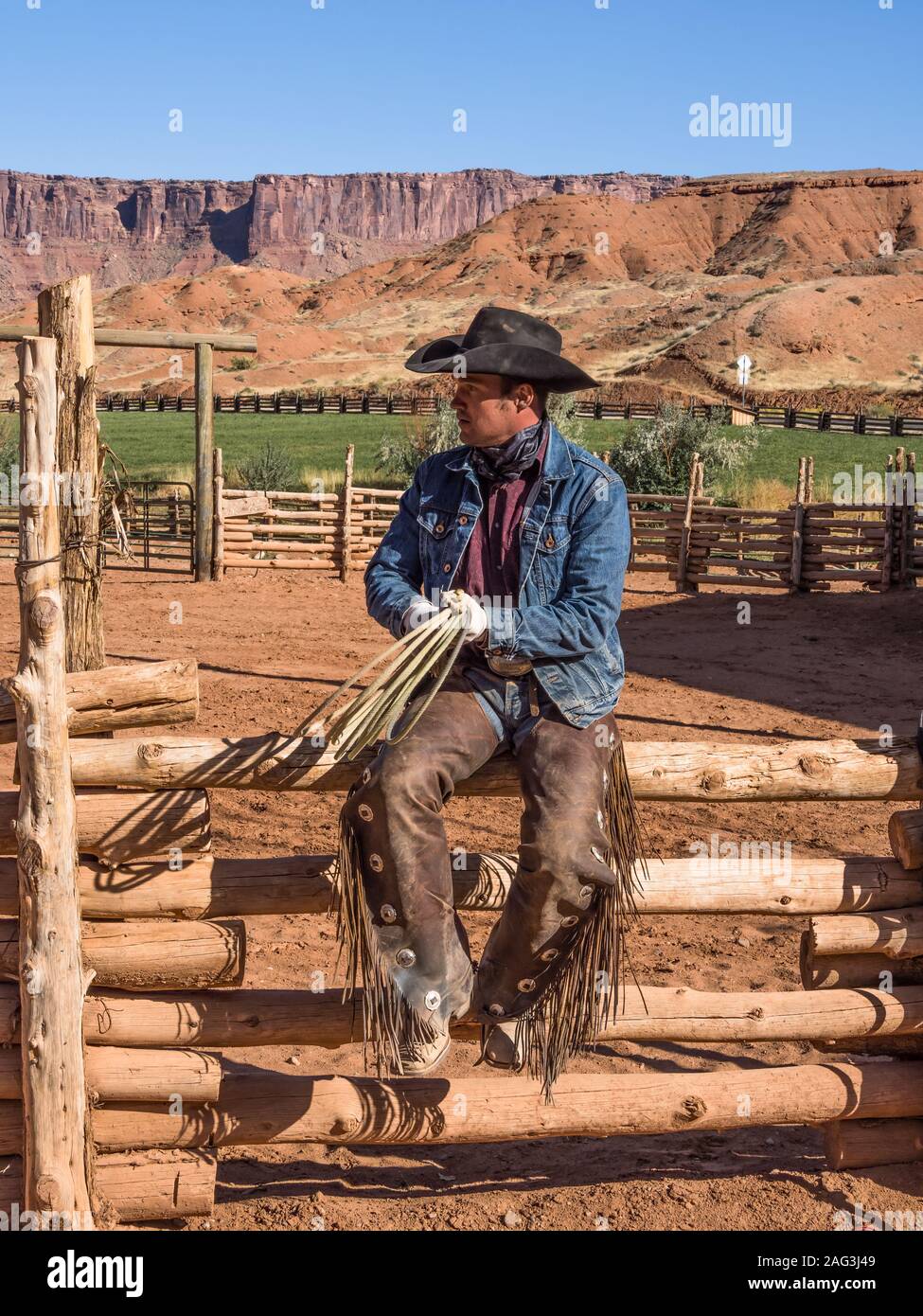 Un cowboy de wrangler pose avec son lariat sur les falaises rouges ranch près de Moab, Utah. Derrière sont les falaises de grès du canyon du Colorad Banque D'Images