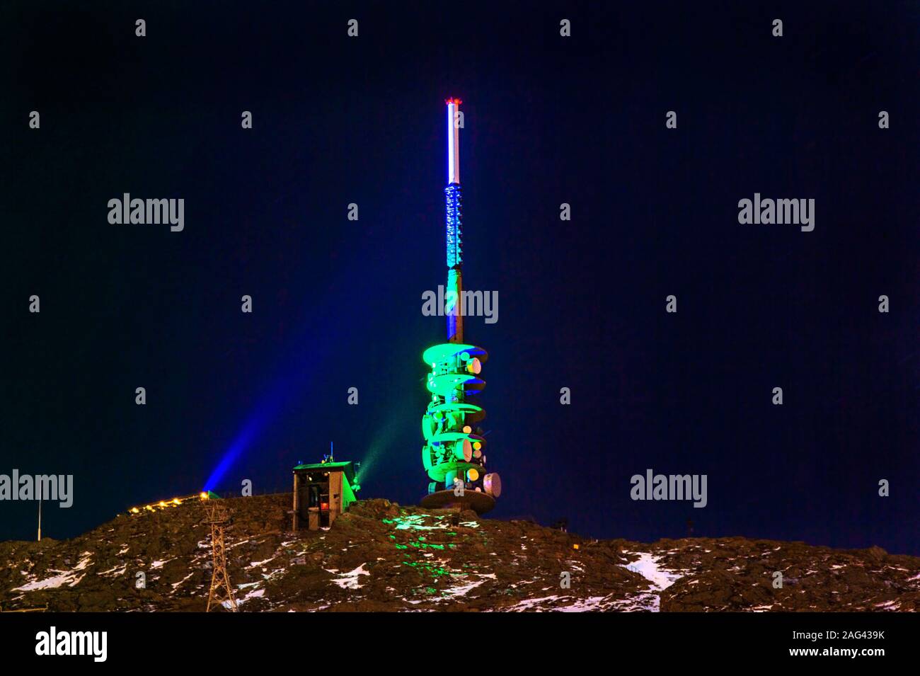 L'antenne TV Tower au sommet d'une montagne éclairée par une lumière colorée dans la nuit. Banque D'Images