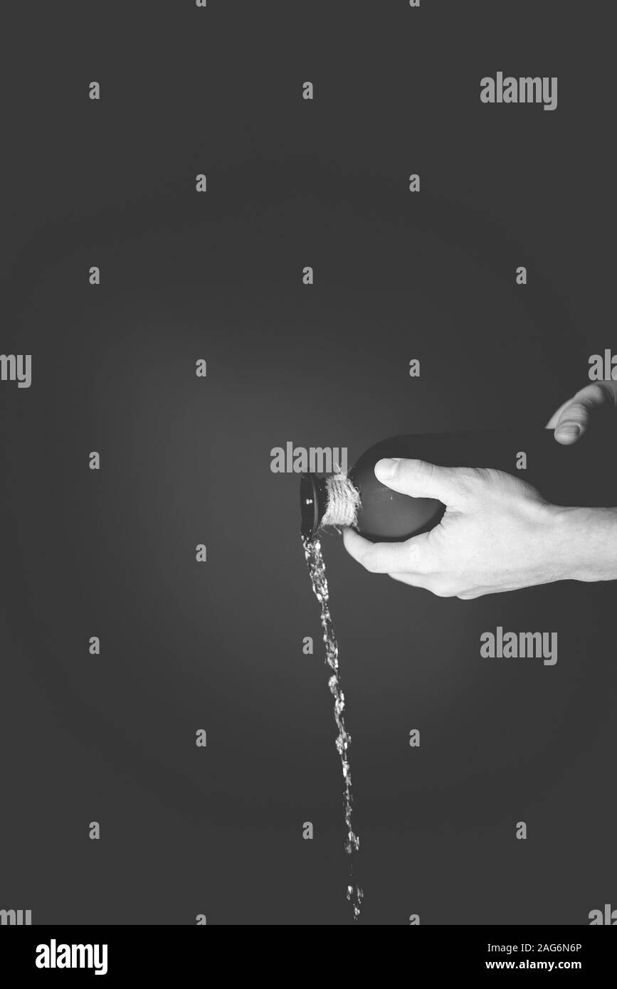 Photo verticale en niveaux de gris d'une personne qui verse de l'eau une bouteille noire Banque D'Images