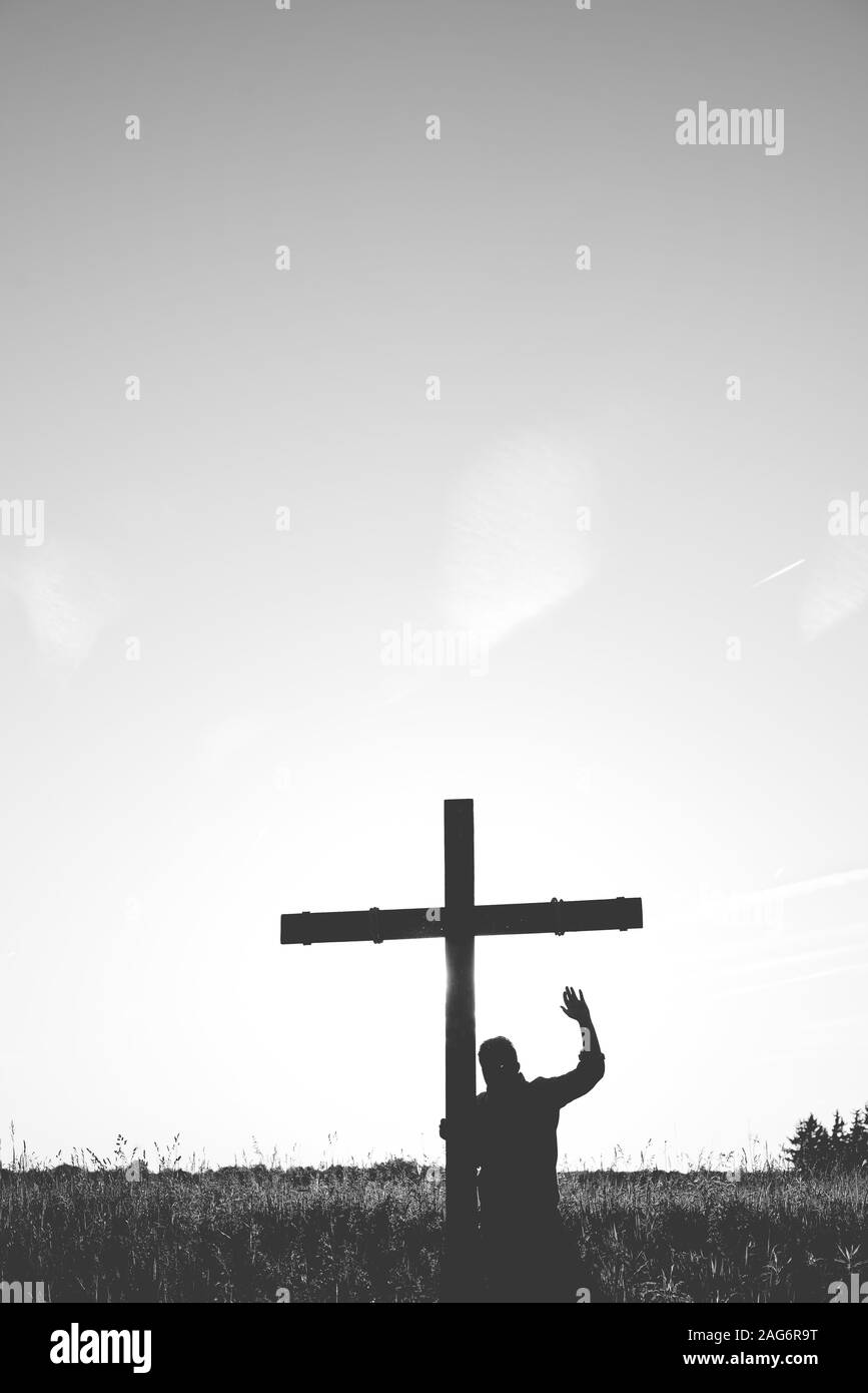 Plan vertical d'un homme se tenant près d'une croix avec sa main en noir et blanc Banque D'Images