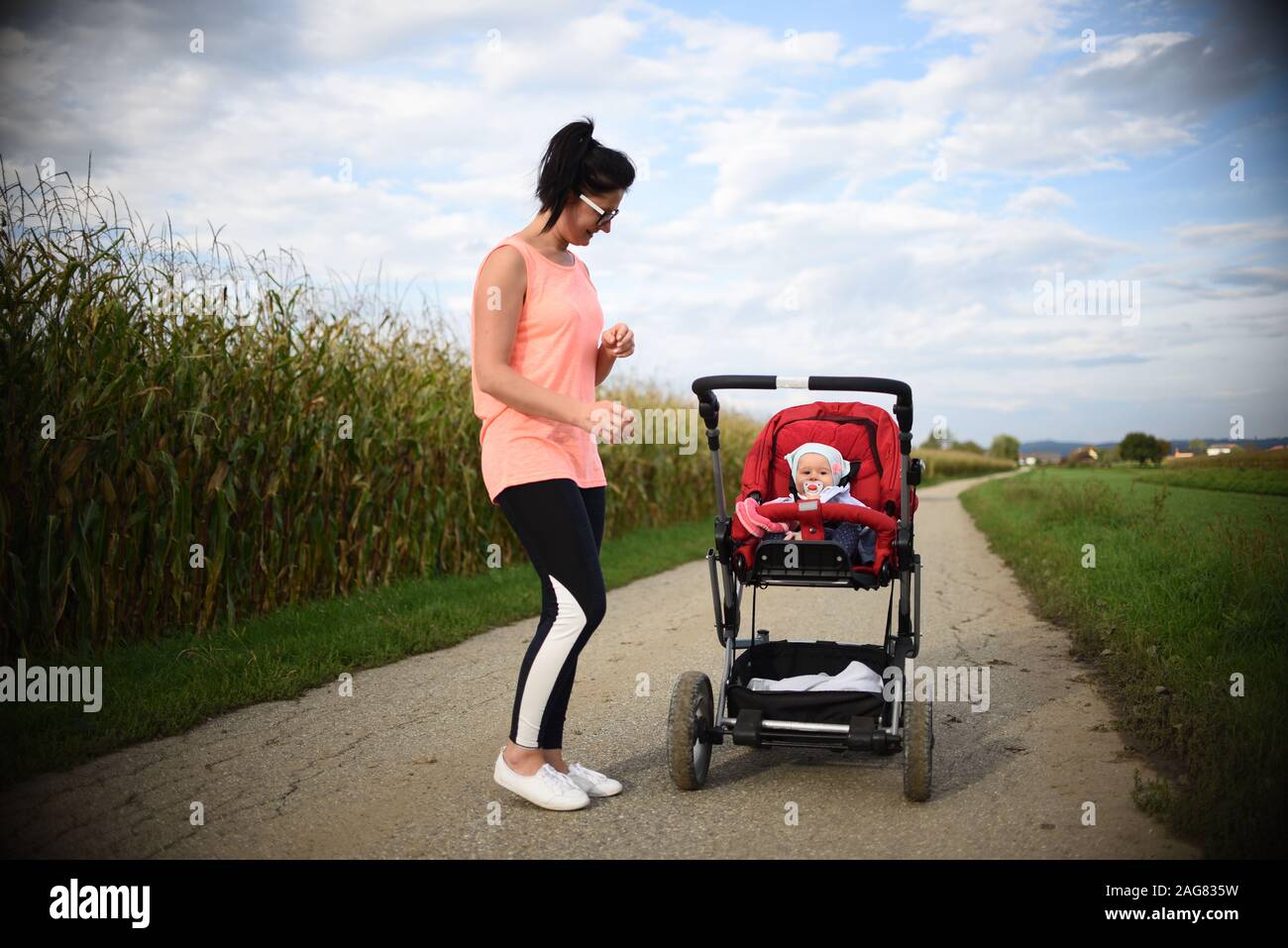 Adorable baby girl à l'extérieur en rouge poussette dans les champs avec sa mère. Sucette nouveau-né avec. Banque D'Images