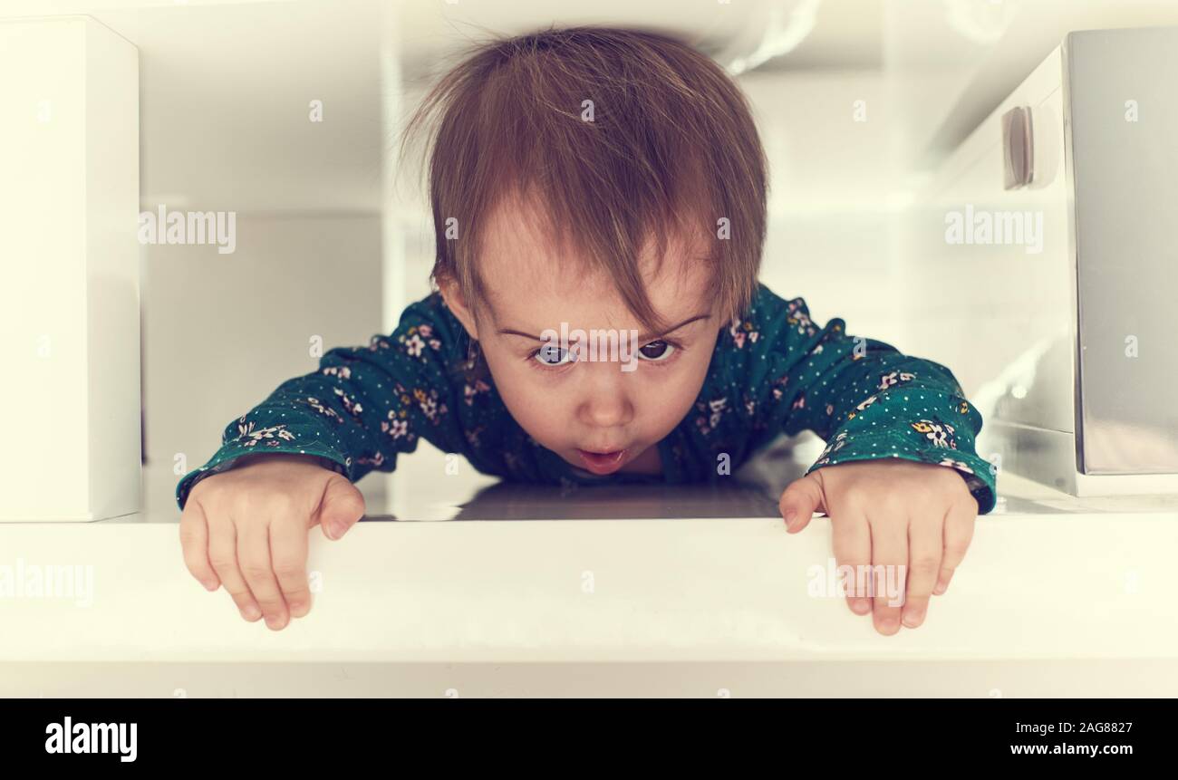 Cute caucasian baby girl ramper dans l'espace serré sous table basse vers la caméra Banque D'Images