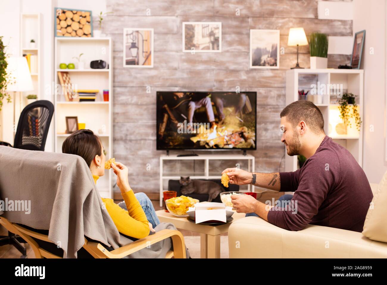 Vue arrière du couple dans le salon à regarder un film sur le téléviseur tout en mangeant de la nourriture à emporter Banque D'Images