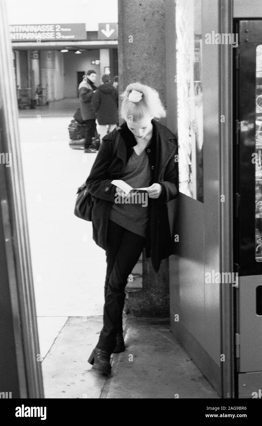 Jeune femme lisant un livre DANS LA GARE MONTPARNASSE PARIS TOUT EN ATTENDANT SON TRAIN - ' FLEUR DE LECTURE' - PARIS - Femme - ARGENT PHOTOGRAPHIE DE RUE FILM © Frédéric Beaumont Banque D'Images