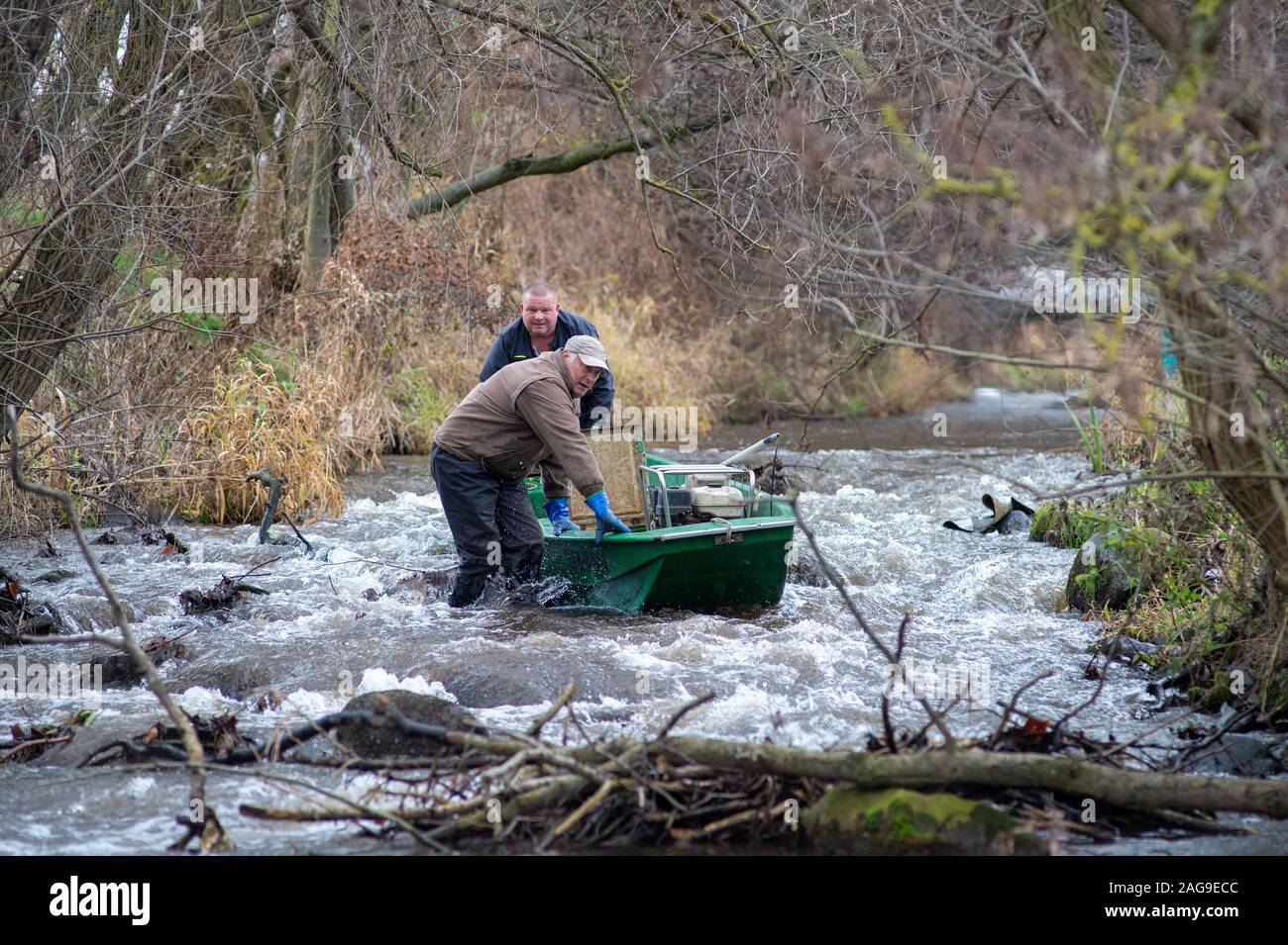 Nutha, Allemagne. Dec 18, 2019. Jens Windheuser (l) et Robert Frenzel (r) de l'Institut des pêches intérieures en Potsdam pousser leur bateau dans la Nuthe sur une faible profondeur. Les pêcheurs doivent effectuer un essai de pêche dans les eaux de l'attraper et de frai de l'étude le saumon et la truite de mer afin de vérifier leur retour. Dans la Nuthe un total de 143500 jeunes saumons et truites de mer 90300 nouveau-nés ont été publiés jusqu'à présent. Les poissons migrent ensuite vers l'Atlantique et revenir frayer après quelques années. Credit : Klaus-Dietmar Gabbert/dpa-Zentralbild/ZB/dpa/Alamy Live News Banque D'Images