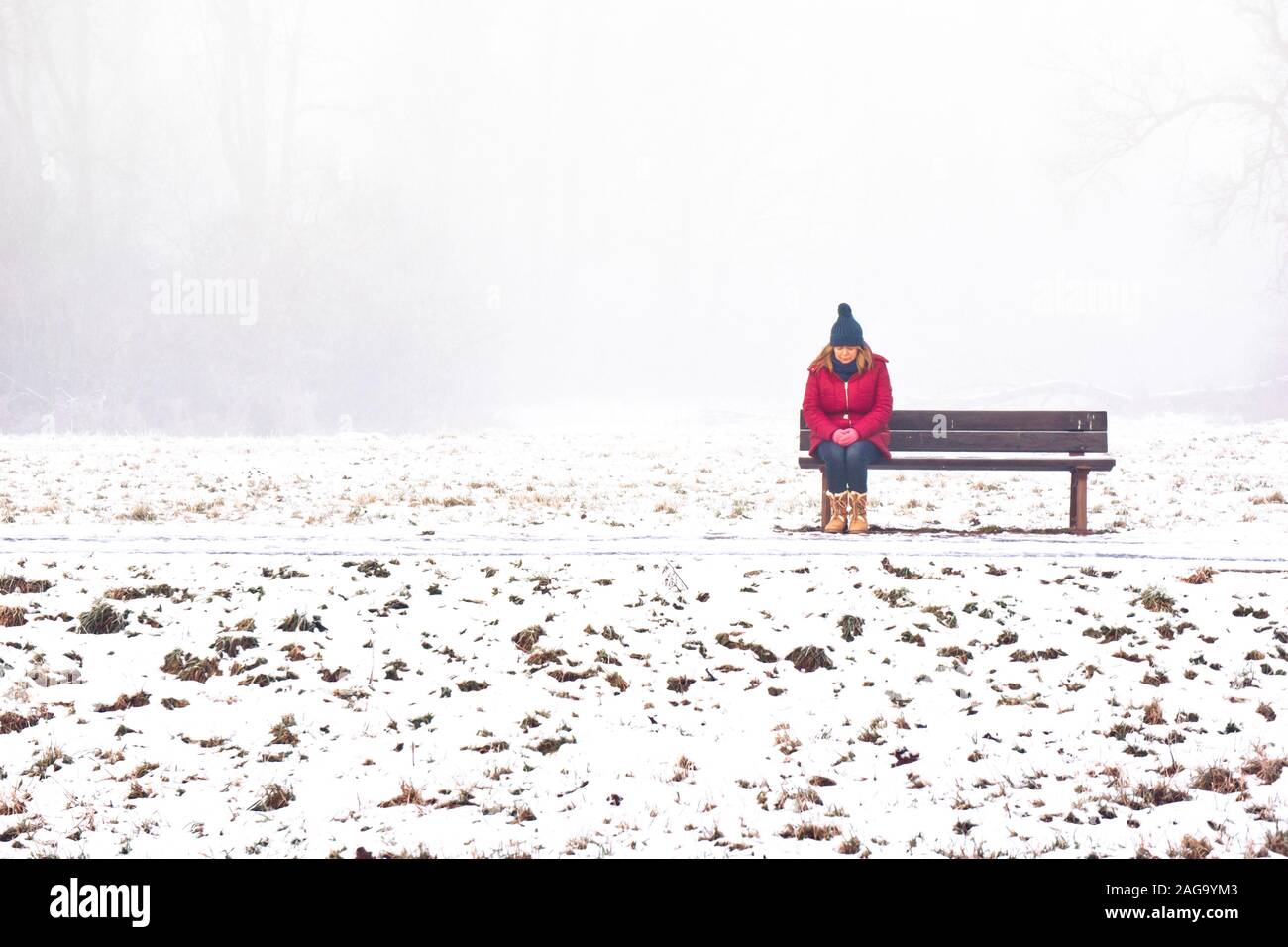 femme avec manteau rouge et chapeau bleu assis sur un seul banc, en hiver neige Banque D'Images