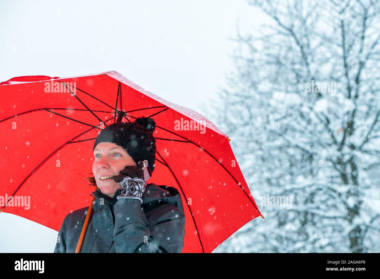 Happy Woman talking on mobile phone sous parapluie rouge tout en se tenant dans la rue en hiver neige Banque D'Images