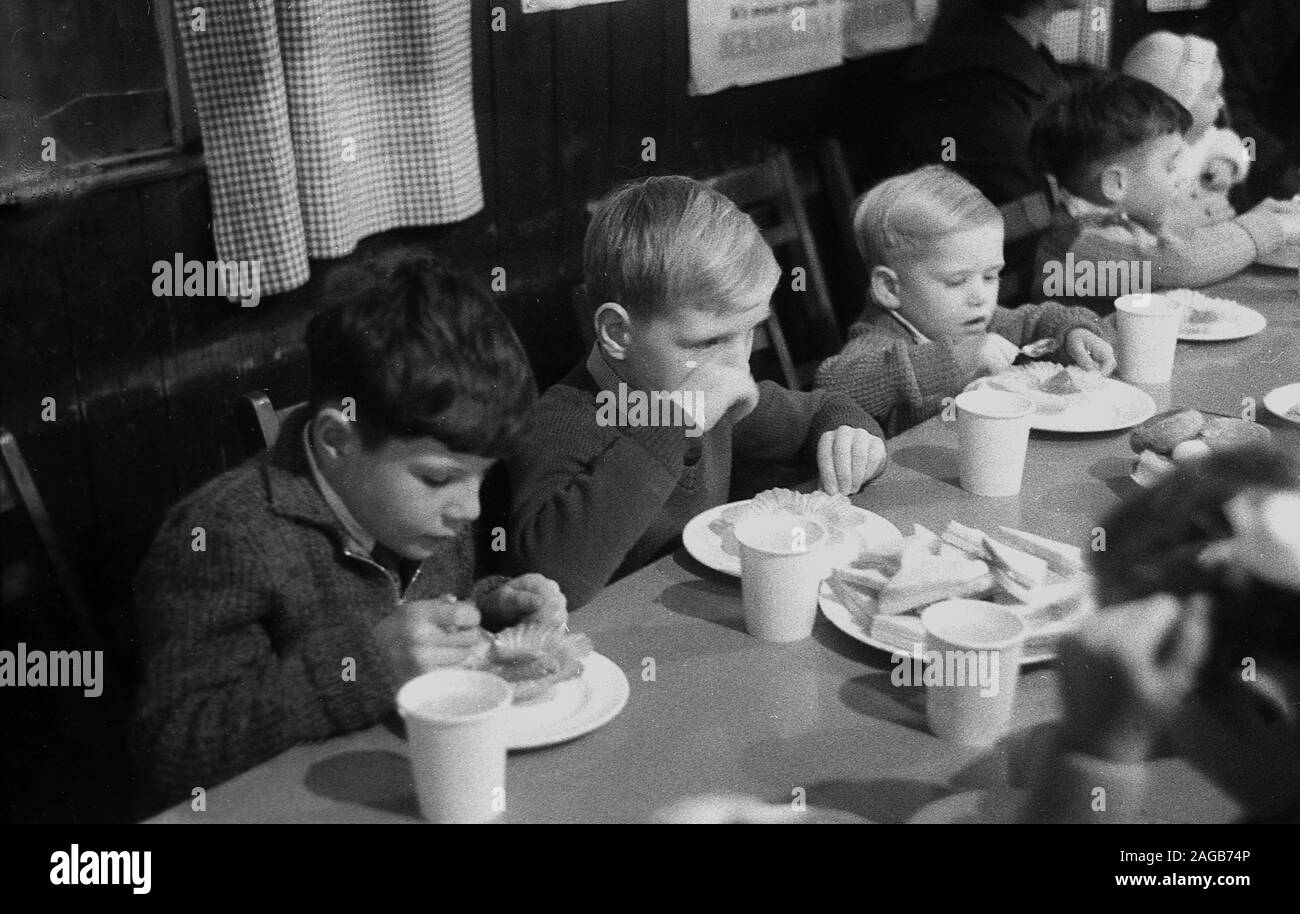 1955, historique, jeunes enfants assis à une table en profitant des sandwichs et des gâteaux à une fête dans une salle de village, Angleterre, Royaume-Uni. Banque D'Images