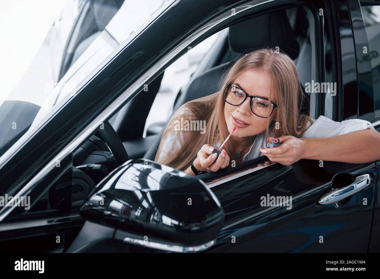 Faire faire par à côté dans le miroir. Belle fille blonde assise dans la  nouvelle voiture avec intérieur noir moderne Photo Stock - Alamy