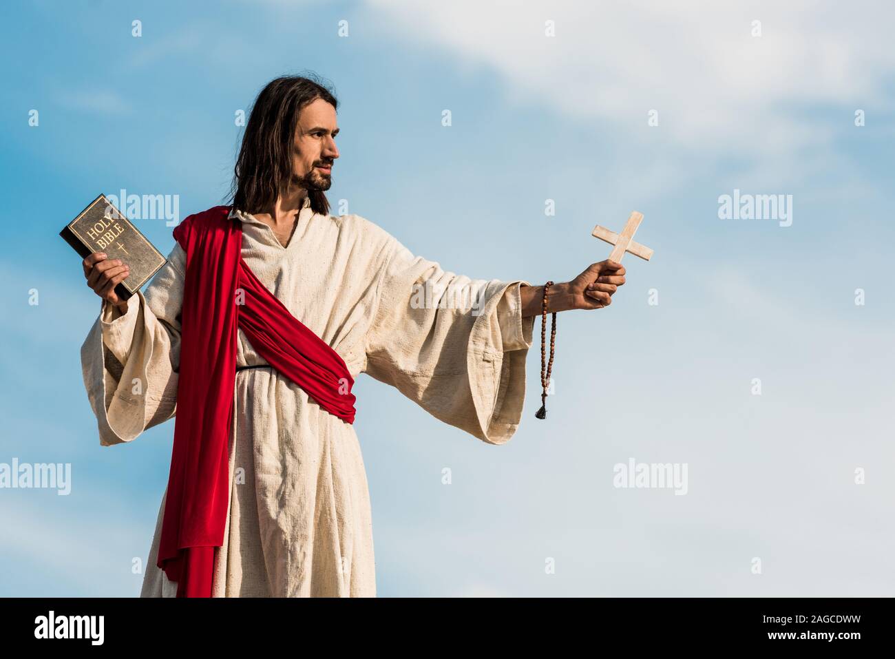 Jésus holding bible sainte Croix et contre le ciel bleu avec des nuages Banque D'Images