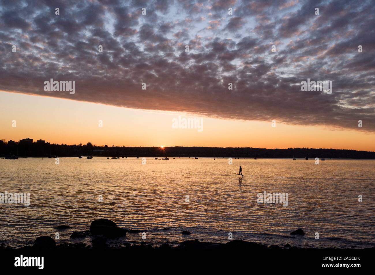 Un surfeur fait une hydroglisseur électrique à travers la baie English, sous un ciel spectaculaire au coucher du soleil à Vancouver, en Colombie-Britannique, au Canada Banque D'Images
