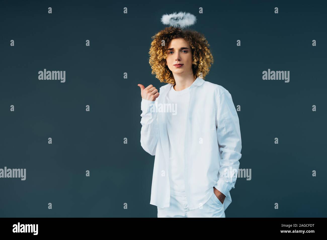 Adolescent bouclés en costume avec halo au-dessus de la tête showing thumb up isolé sur green Banque D'Images