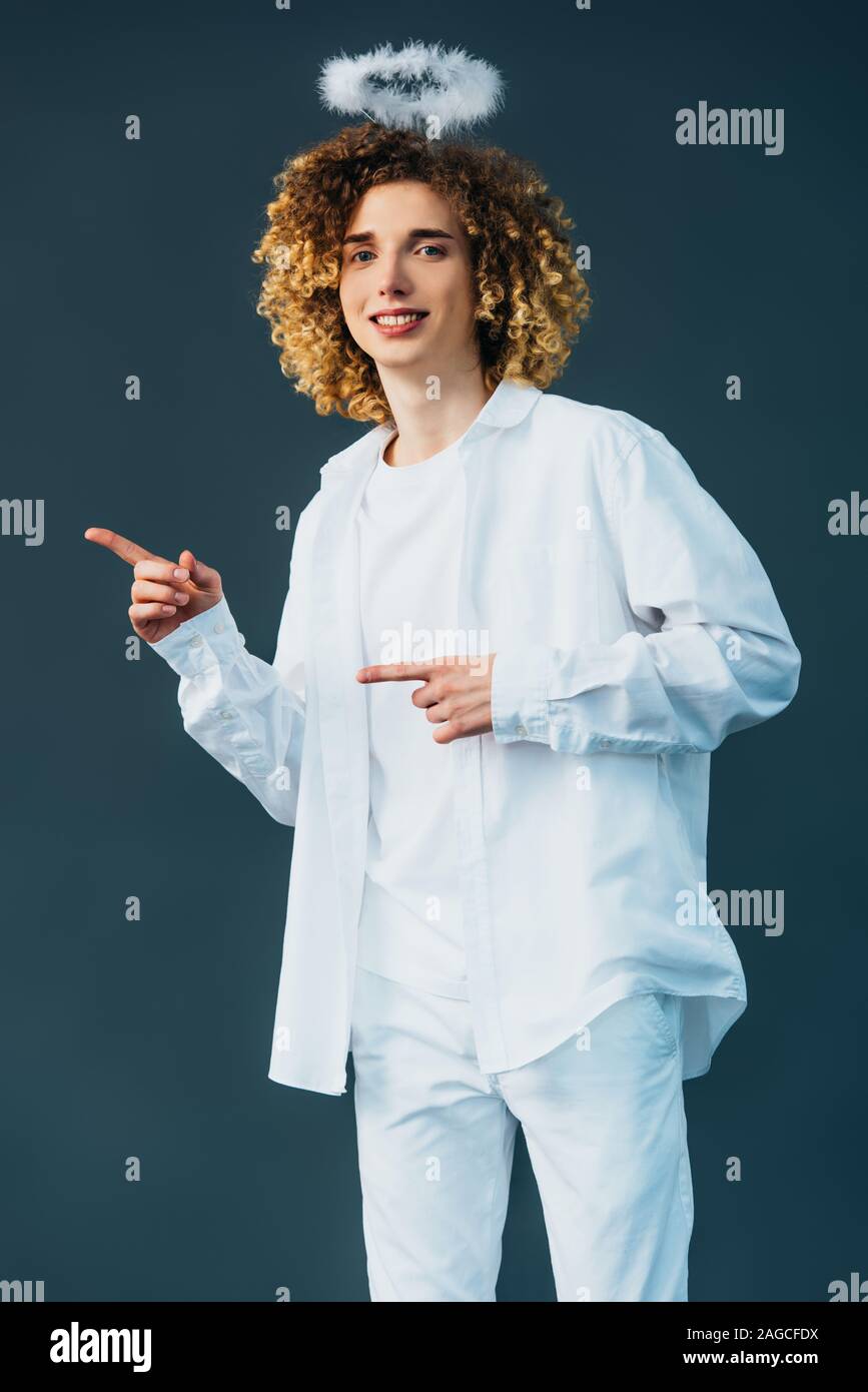 Smiling adolescent bouclés en costume avec halo au-dessus de la tête avec les doigts pointant isolé sur green Banque D'Images