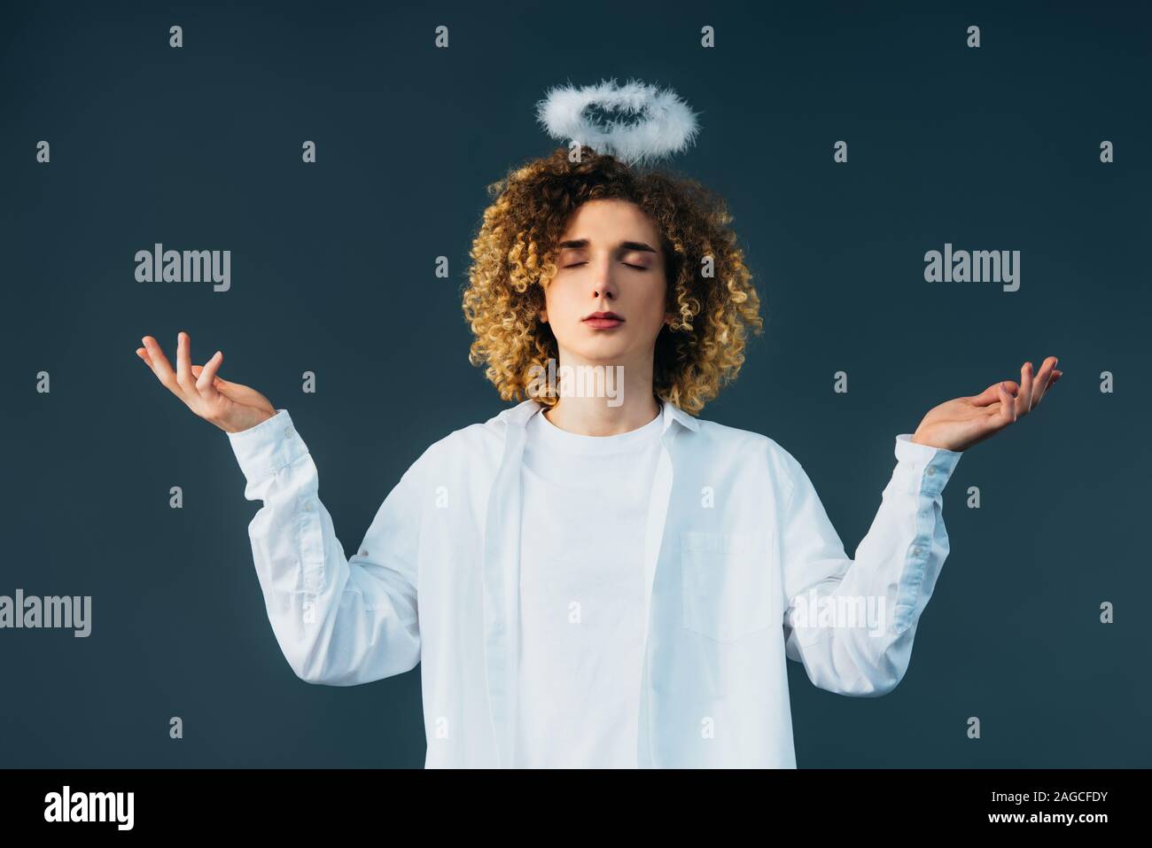 Adolescent bouclés en costume avec halo au-dessus de la tête, yeux clos et mains tendues isolé sur green Banque D'Images