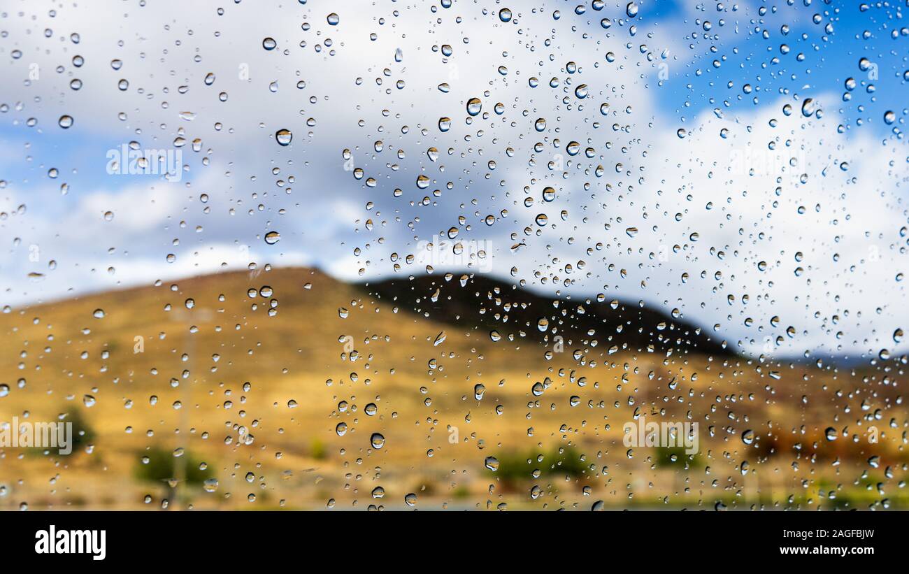 Gouttes de pluie sur la fenêtre sur un jour d'hiver pluvieux dans le comté de Los Angeles, Californie ; troubles de collines couvertes par de l'herbe sèche visible à l'arrière-plan ; sha Banque D'Images