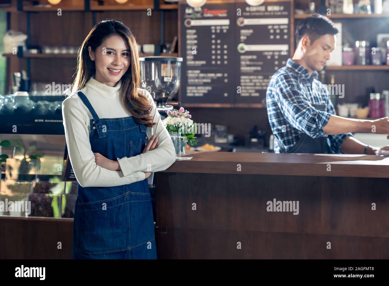 Portrait of young adult asian propriétaire de café cafétéria debout devant barista bar à café avec l'employé qui travaille en arrière-plan. À l'aide d'e Banque D'Images