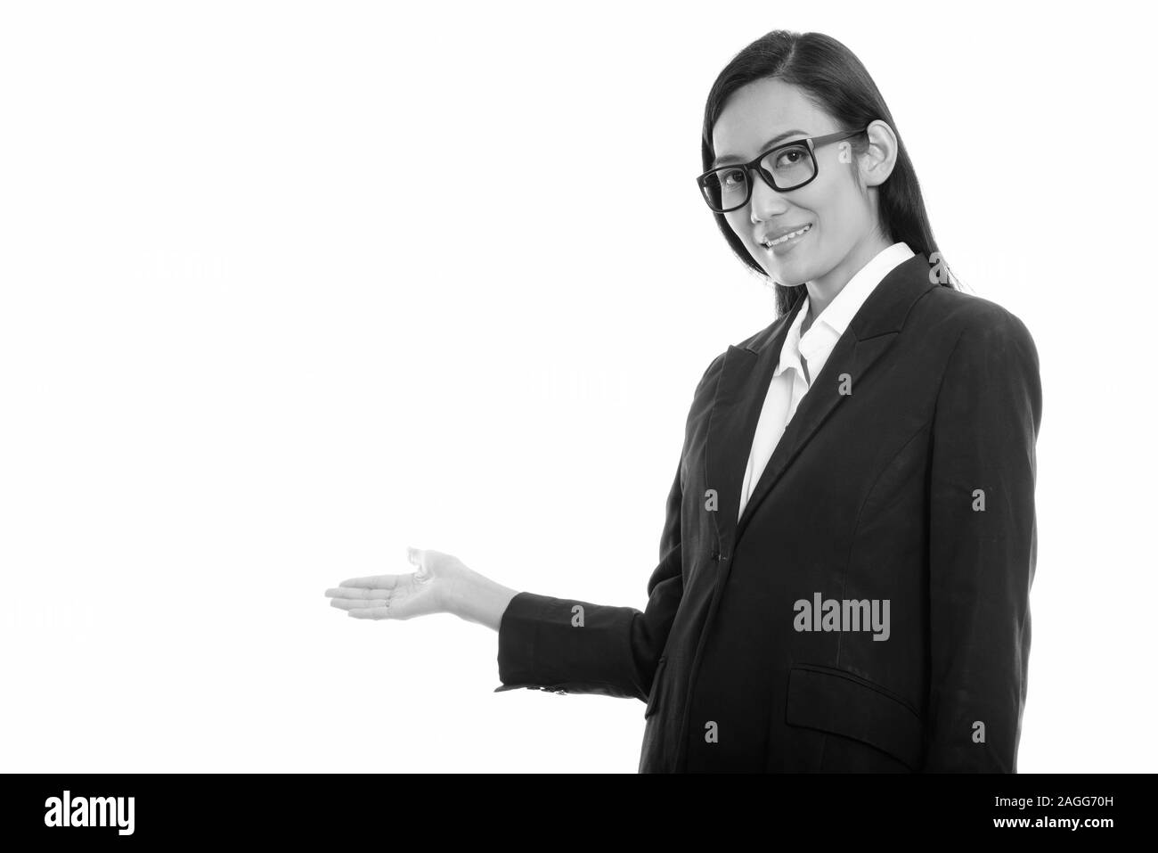 Studio shot of young happy Asian businesswoman smiling tout en montrant quelque chose Banque D'Images