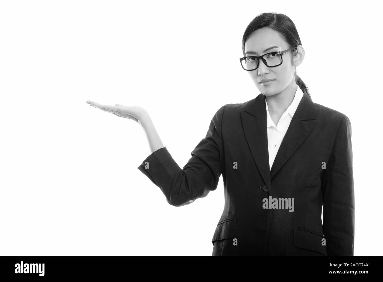 Studio shot of young Asian businesswoman wearing eyeglasses tout en montrant quelque chose Banque D'Images
