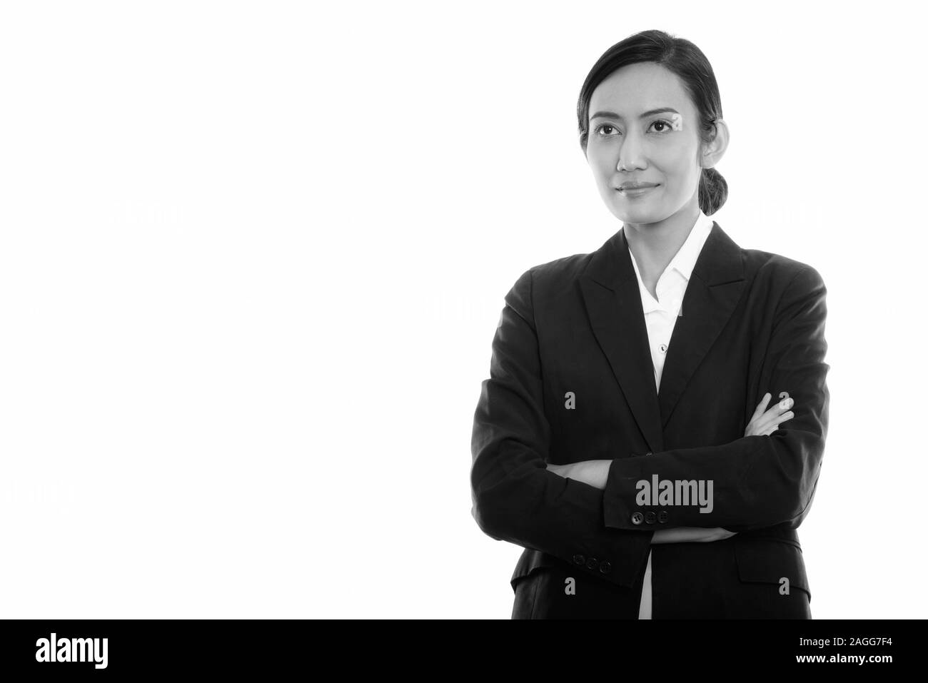 Studio shot of young Asian businesswoman thinking, tout en regardant vers le haut avec les bras croisés Banque D'Images