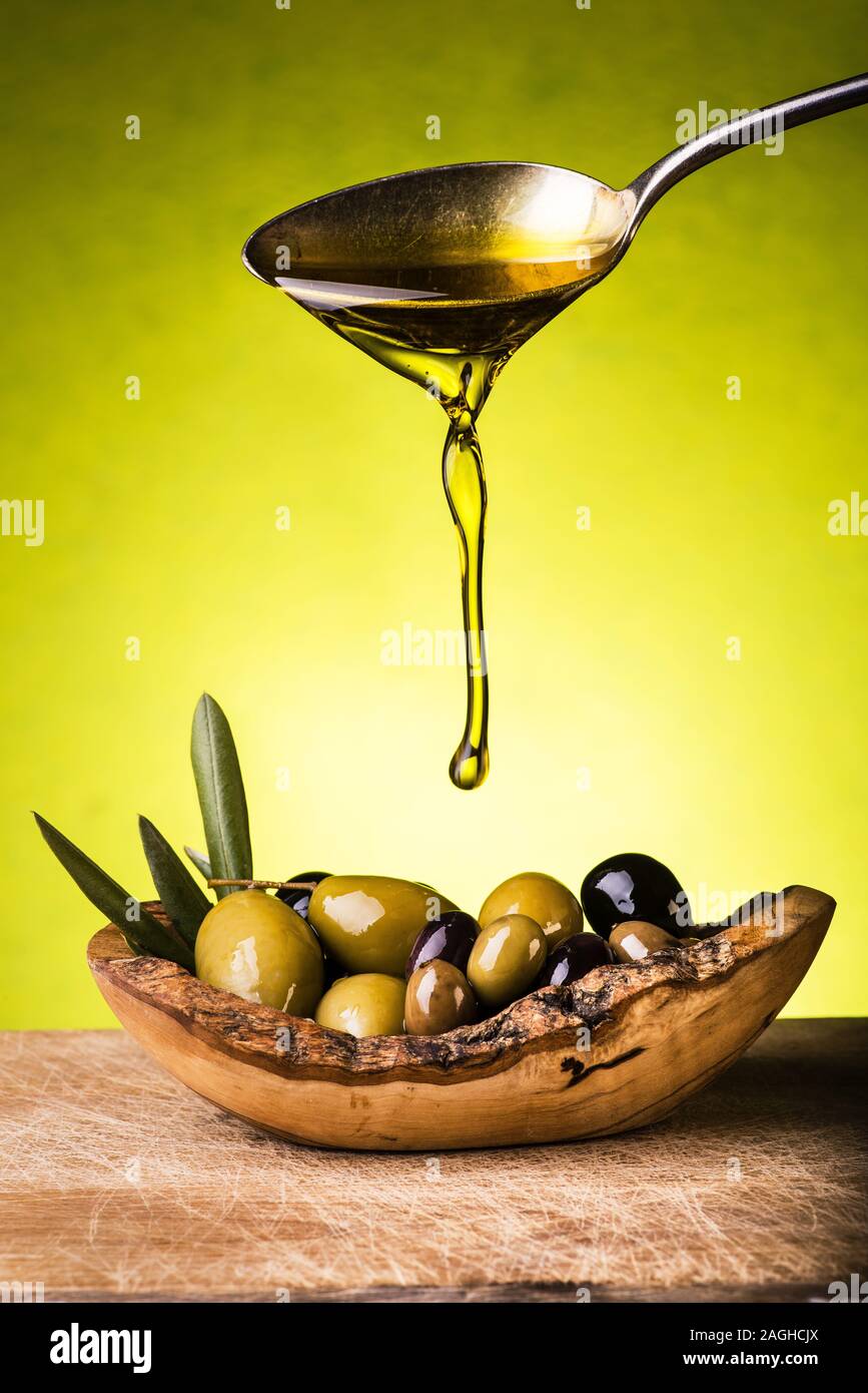 Une cuillerée d'huile est versé sur le bol contenant différents types d'olives Banque D'Images