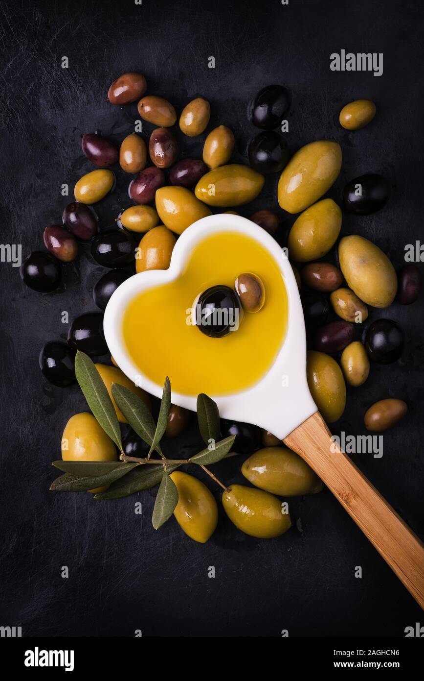 Louche en forme d'un cœur plein d'huile et certains types d'olives sur le fond sombre Banque D'Images
