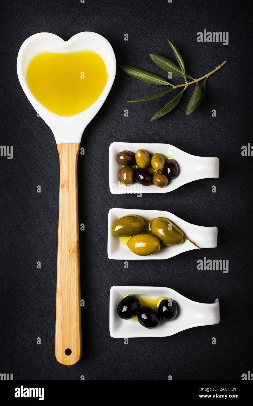 Louche en forme d'un cœur plein d'huile et certains types d'olives sur le fond sombre Banque D'Images