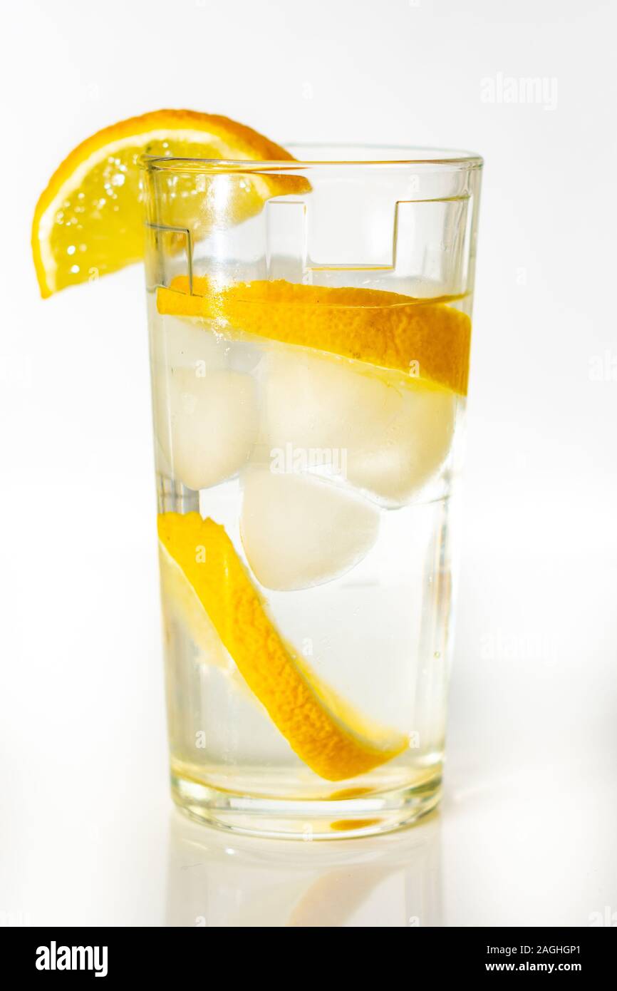 Verre d'eau avec de la glace et des tranches de citron sur un fond blanc. Banque D'Images