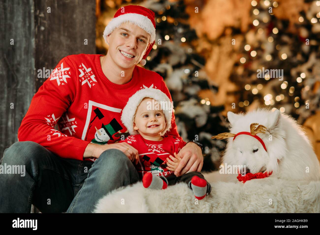 Père et petit fils au Père Noël chapeaux s'asseoir à côté de chien samoyède  blanc contre l'arrière-plan de l'arbre de Noël et décorations Photo Stock -  Alamy