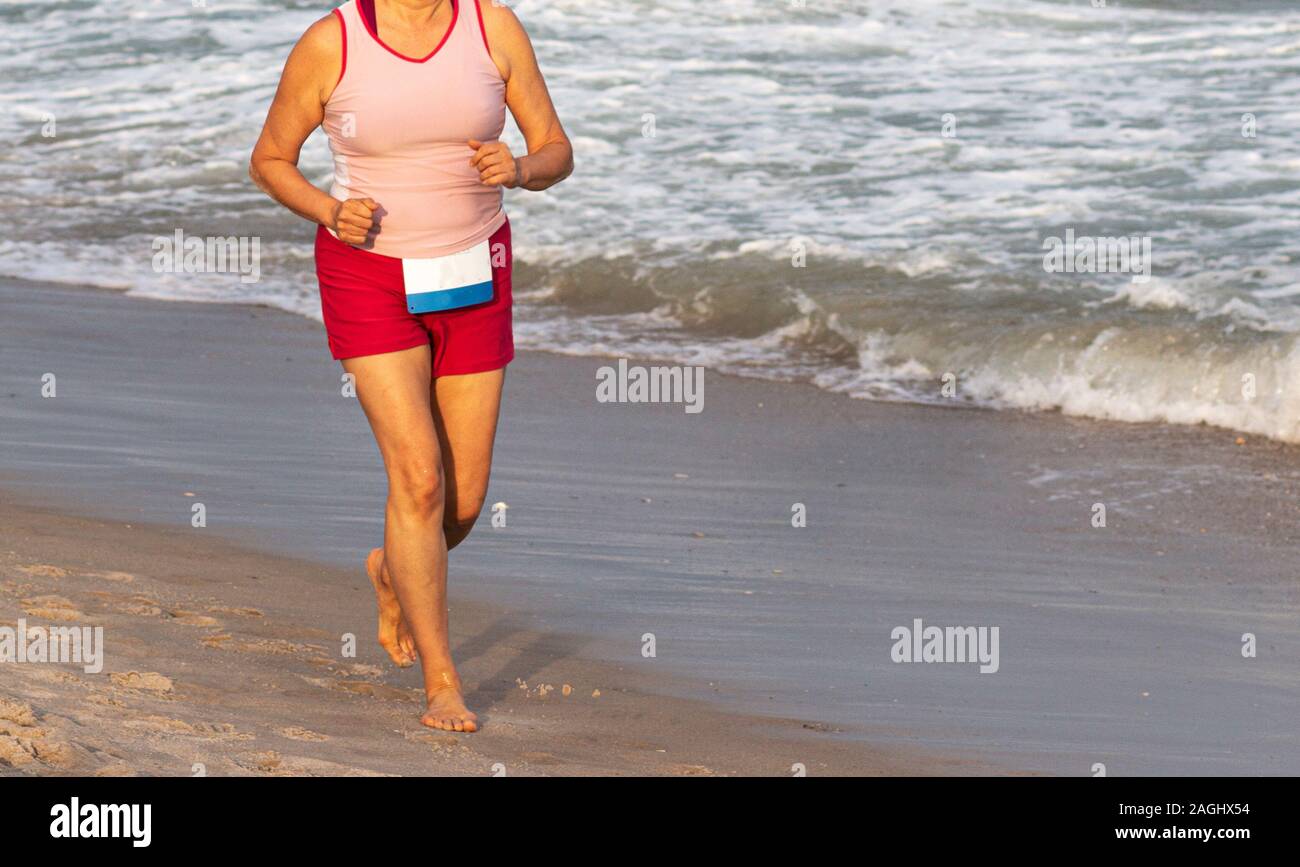 Une femme est en cours d'exécution une course sans chaussures sur le sable de la plage au bord de l'océan. Banque D'Images