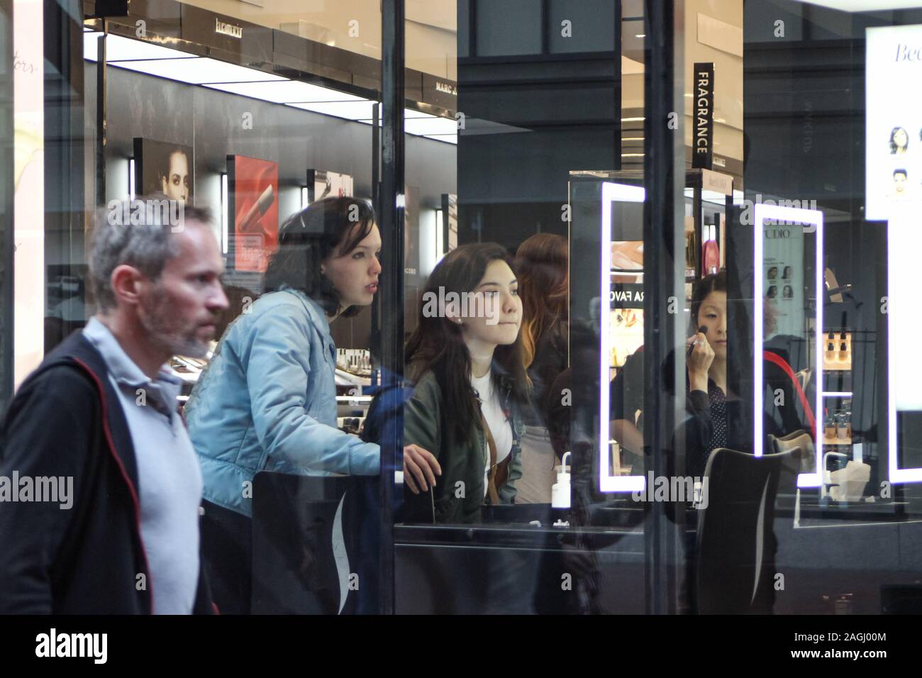 Les jeunes femmes ou adolescentes à beauty store vue à travers la fenêtre de la boutique. Homme d'âge moyen passant sur Powell Street, San Francisco, États-Unis. Banque D'Images
