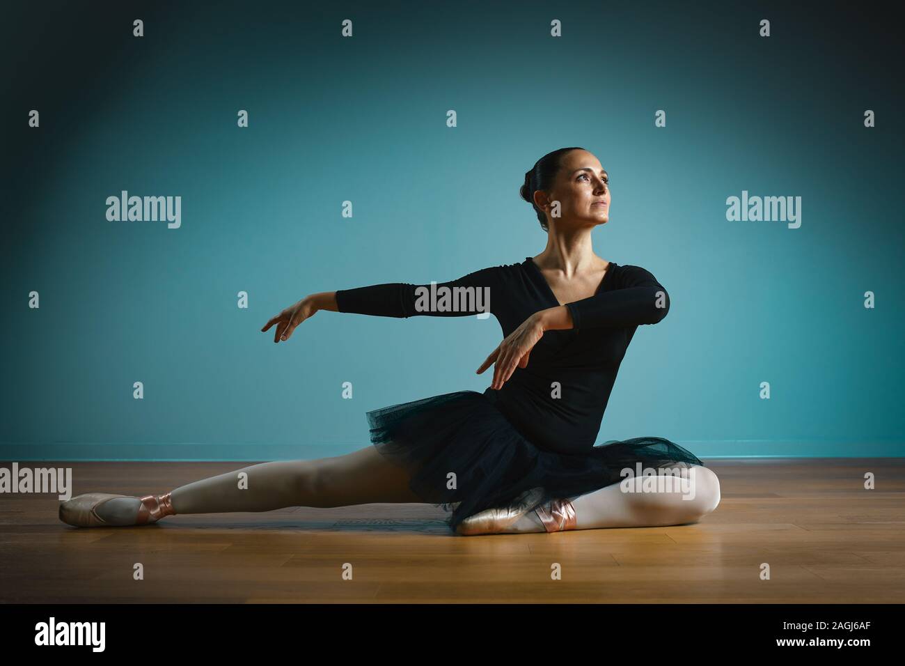 Jolie femme ballerine en tutu et pointe en noir Maillot de posing in studio sur fond bleu. Banque D'Images