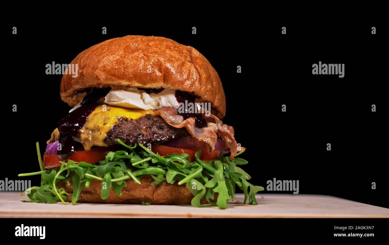Burger d'artisanat est cuisson sur fond noir. Composé : sauce, roquette, tomate, oignon, bacon, fromage ricotta, sauce au cassis, pain d'air et en viande. Banque D'Images Burger d'artisanat est cuisson sur fond noir. Composé : sauce, roquette, tomate, oignon, bacon, fromage ricotta, sauce au cassis, pain d'air et en viande. Banque D'Images