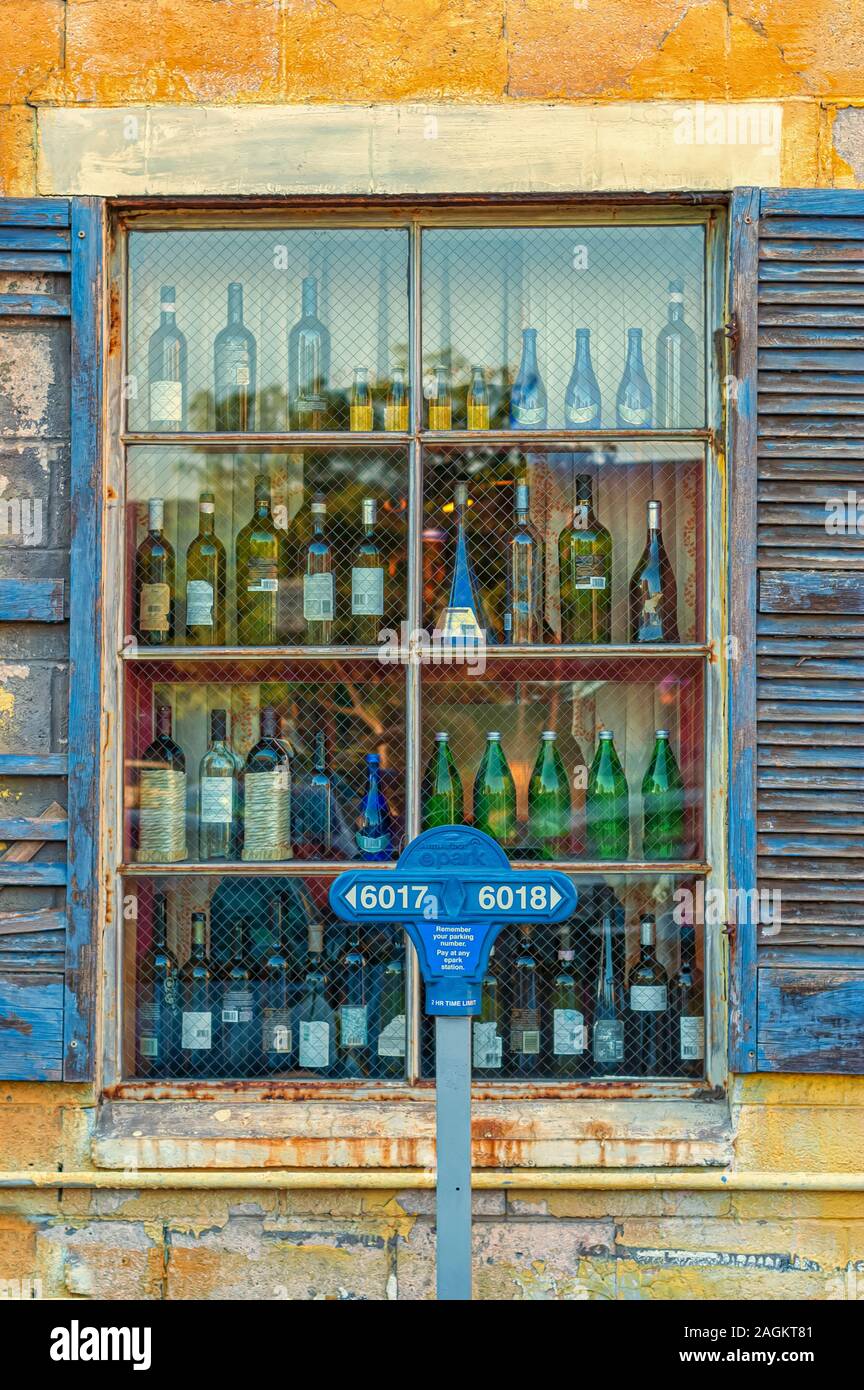 Un parcomètre en dehors de la fenêtre d'un restaurant affichant de nombreuses bouteilles de vin vide comme objets de décoration. Banque D'Images