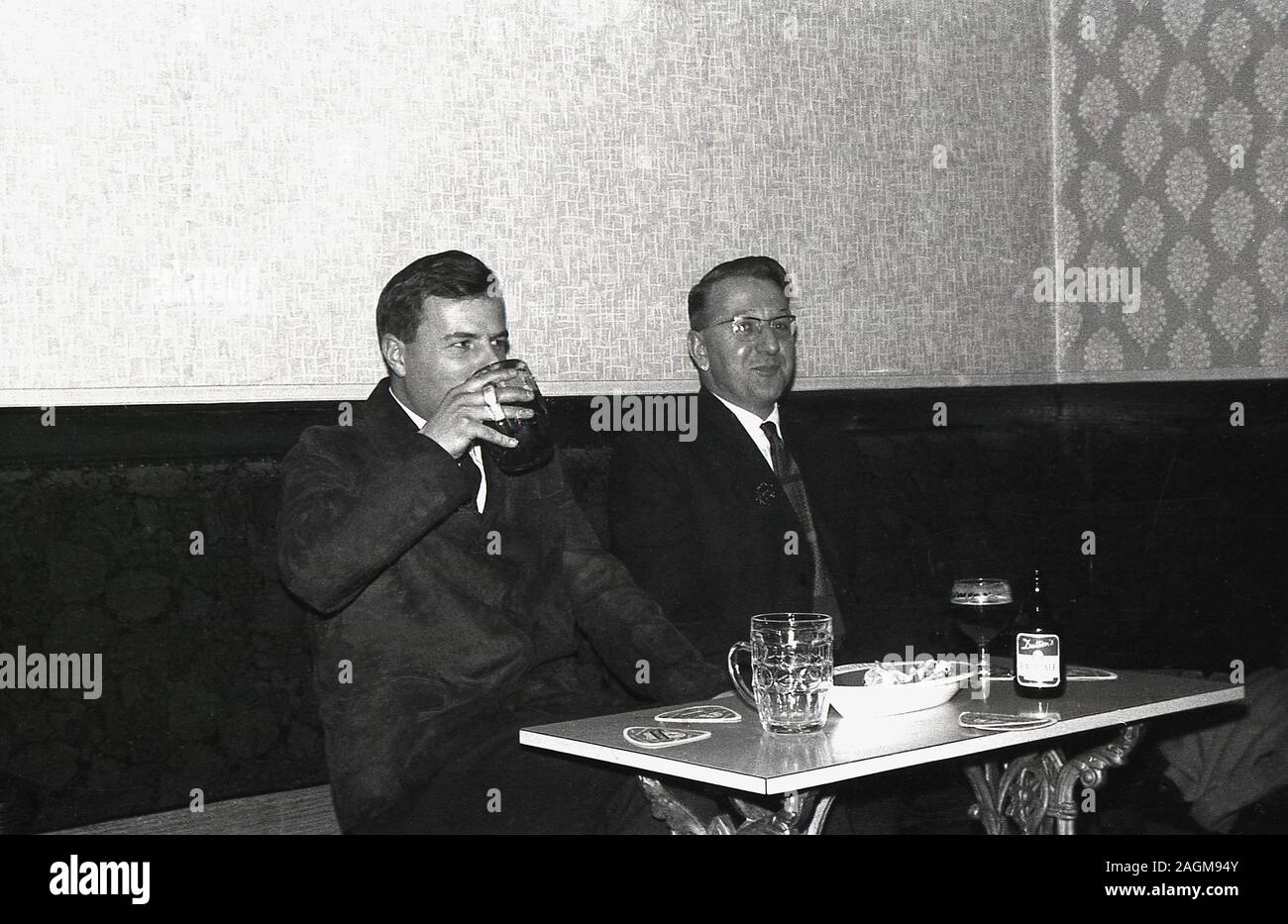Années 1960, historiques, deux hommes bien habillés assis dans un coin d'un bar ou pub, boire de la bière, avec l'un d'entre eux ayant une bouteille de Dutton's Pale Ale, England, UK. Banque D'Images