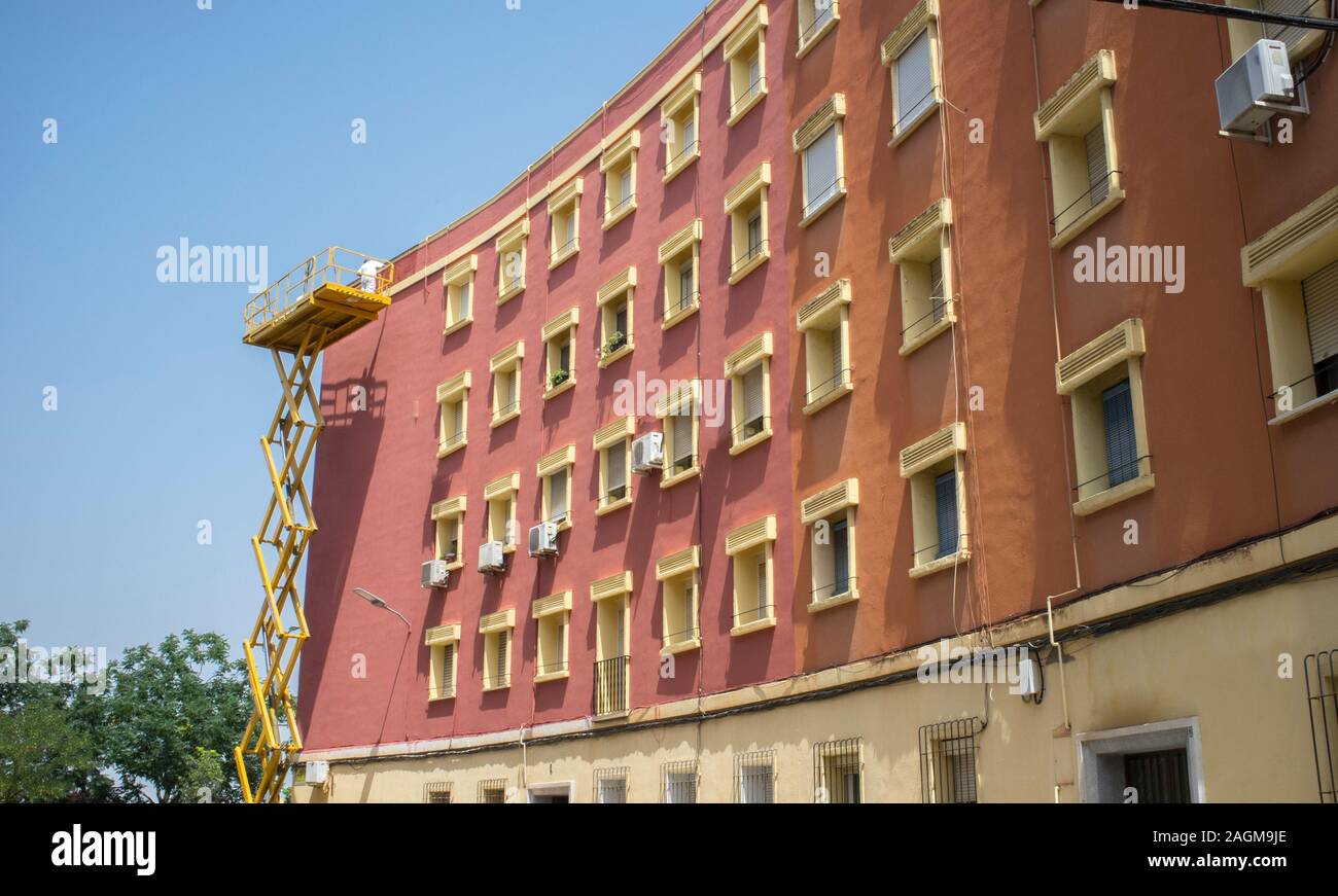 Travail peintre sur la plate-forme élévatrice à ciseaux. Ciel bleu sur fond urbain Banque D'Images