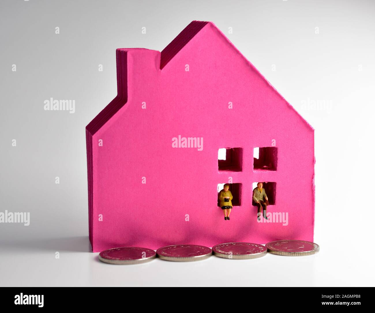 Couple retraité miniature, assis sur une petite maison, avec un toit rouge Banque D'Images