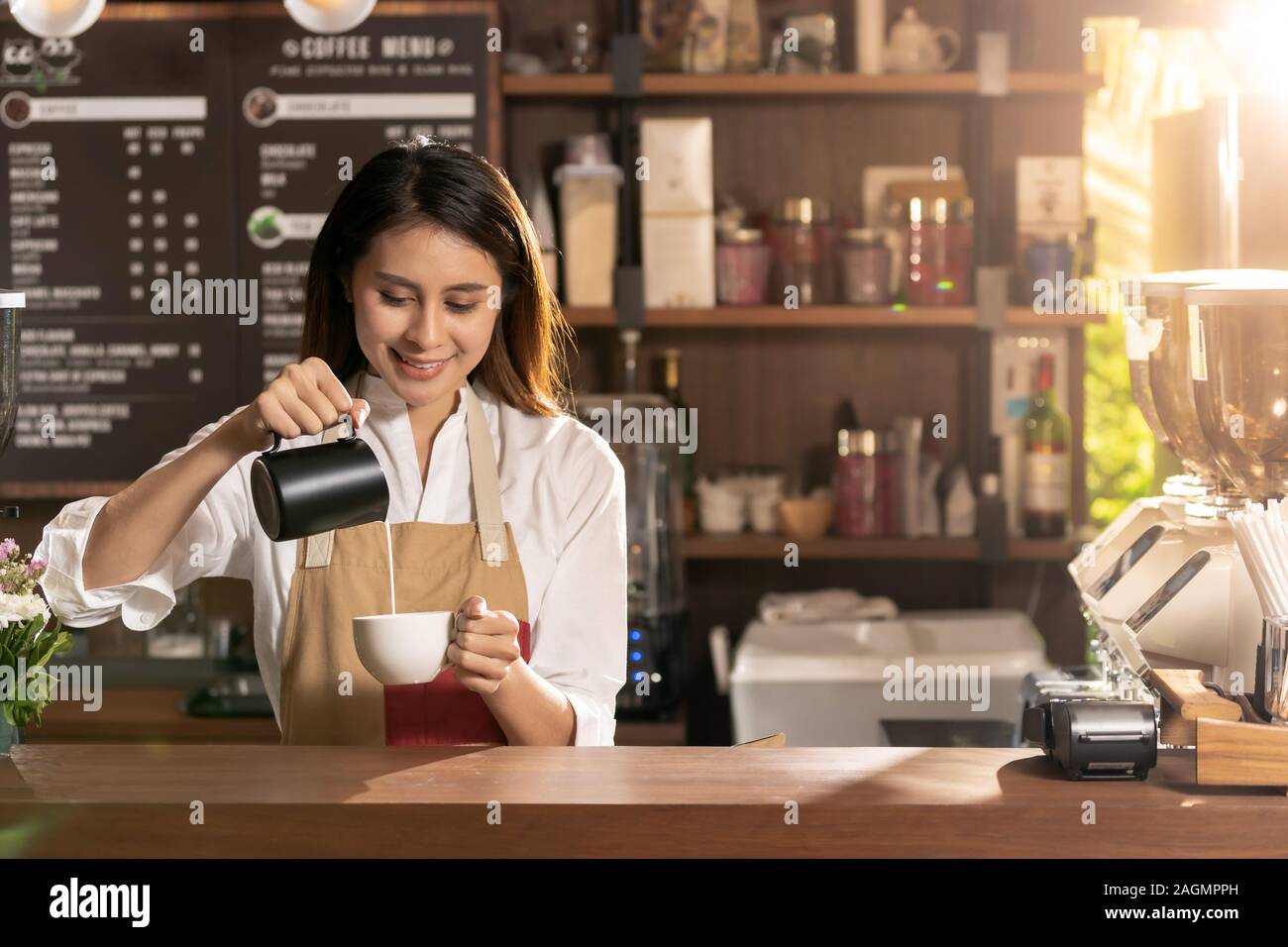 Young adult asian female barista pouring lait frais pour préparer du café latte pour client dans un café-bar. Banque D'Images